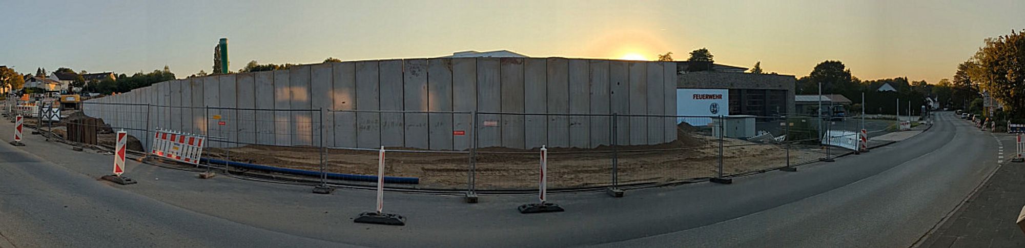 Eine Stützmauer entlang einer Straße. Der Blick auf die untergehende Sonne ist von der hohen Mauer verdeckt.