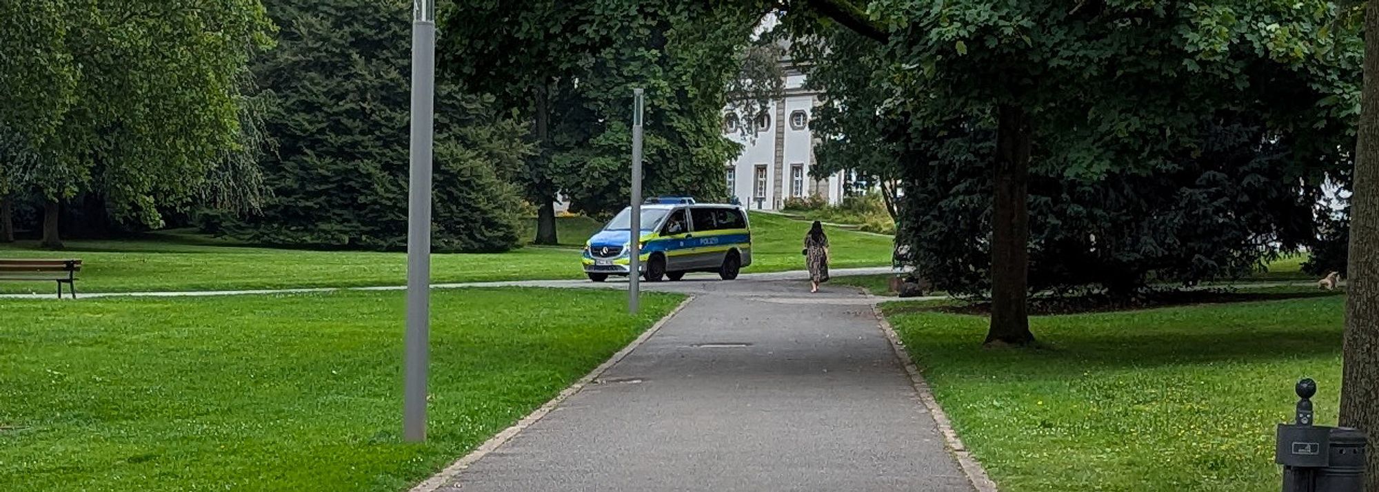 Ein Polizeibulli fährt auf den Gehwegen in einem Park Streife.