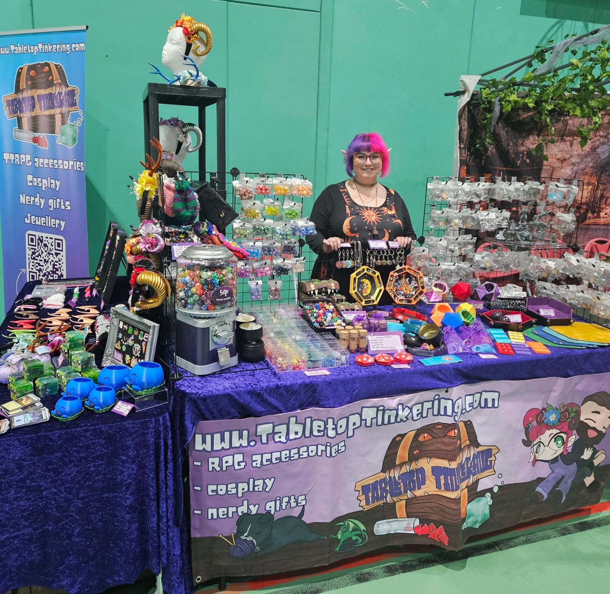 A person with pink and purple hair behind a purple stall covered in gaming accessories