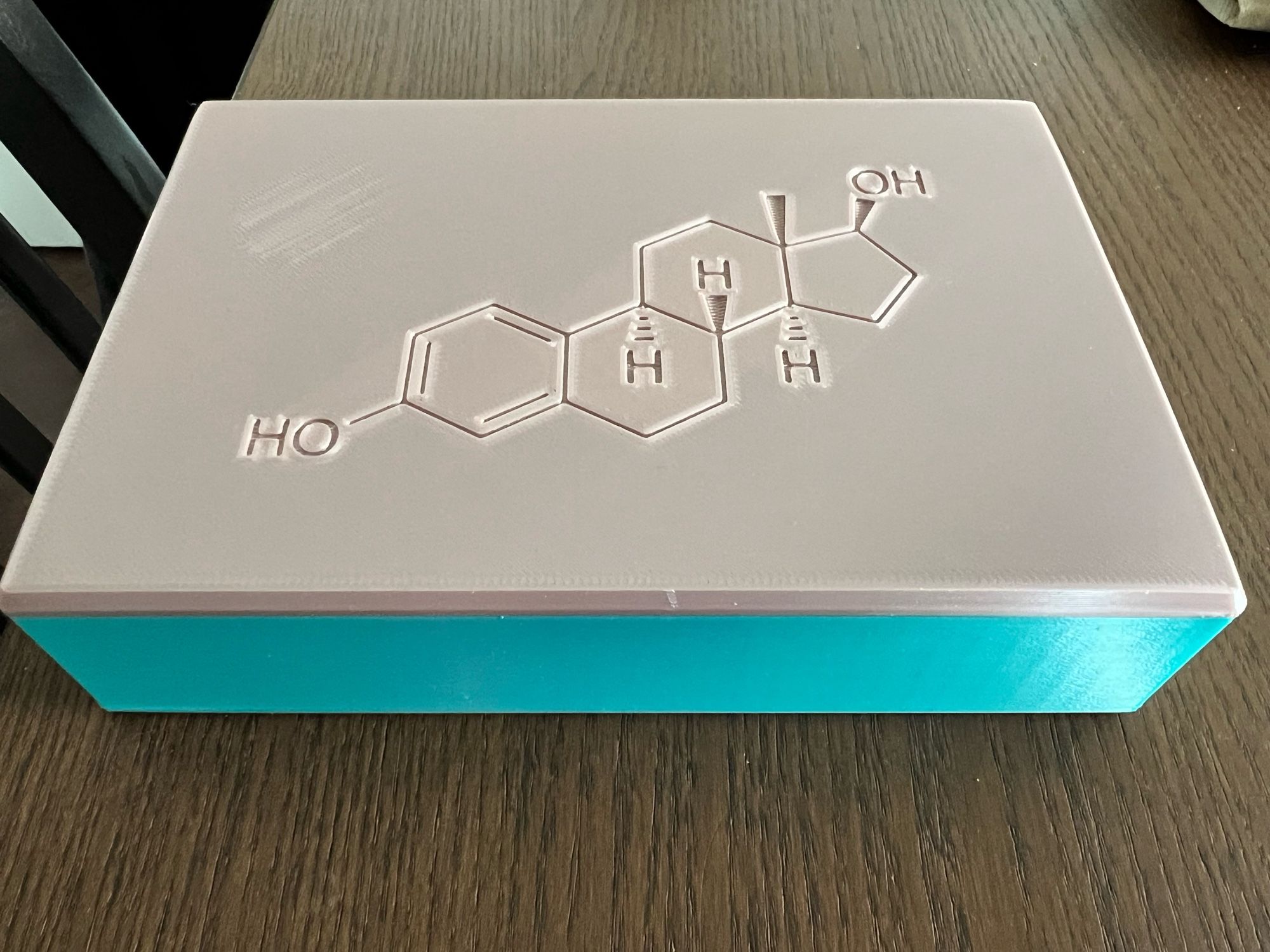 a picture of a plastic rectangle case, with blue base and pinkish top. 

on the top is the chemical symbol for estrogen engraved on it.