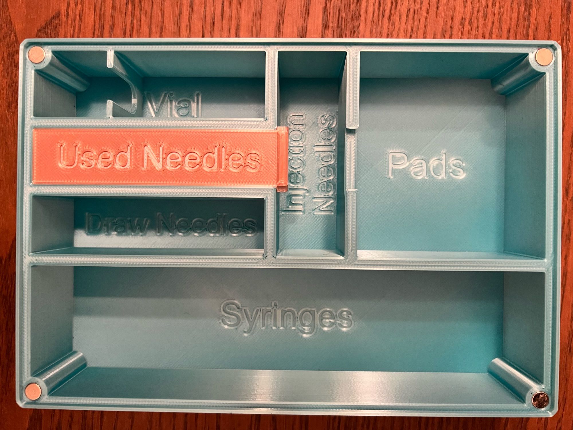 a peek inside the case, with little compartments labeled thusly: Vial, Used Needles (a lid that slides open to hold them), Draw Needles, Injection Needles, Pads, and Syringes