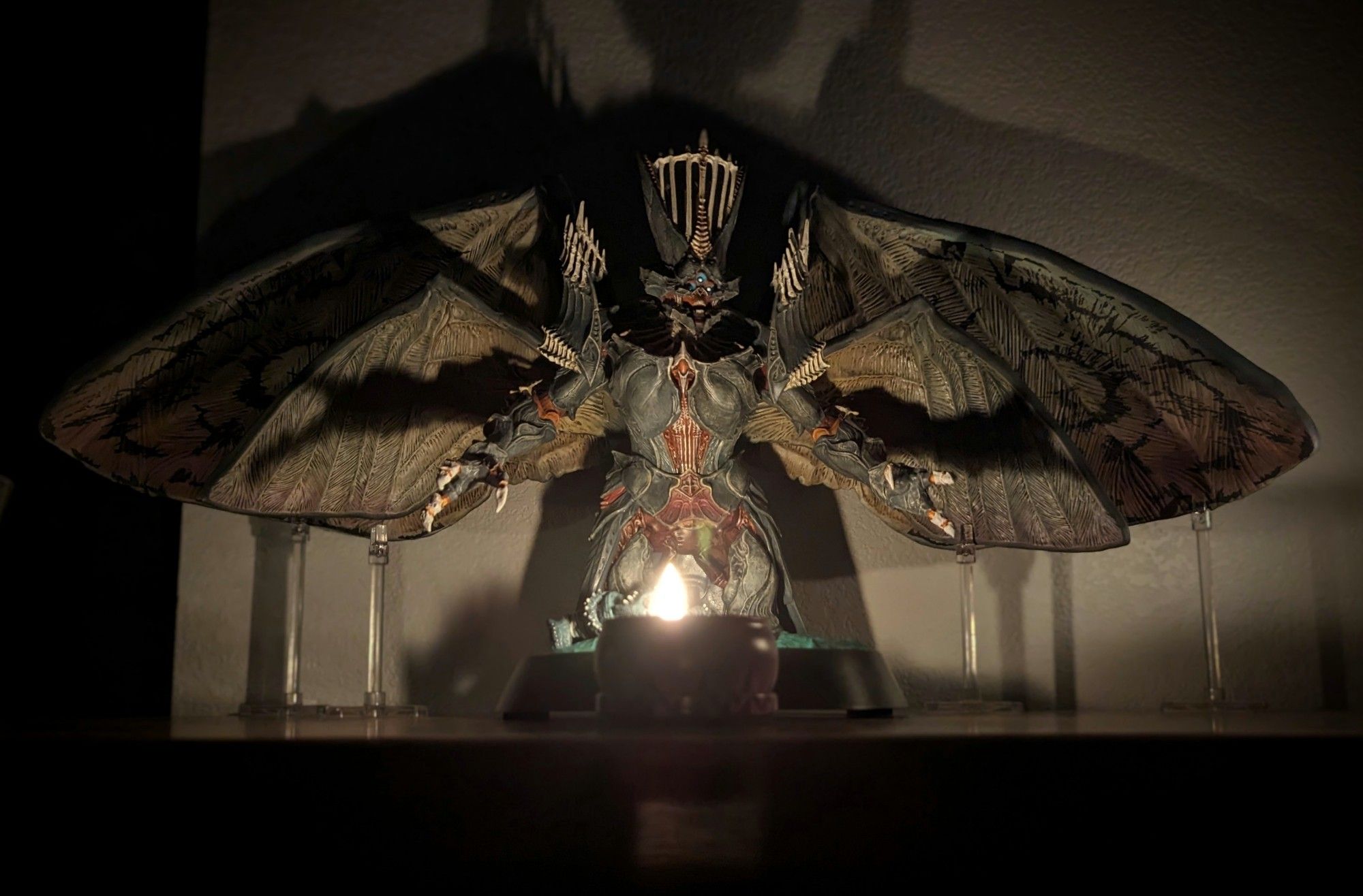 a large figurine of the character Savathun from destiny 2 in a dark room, lit from below by a candle and casting a large shadow on the white wall behind