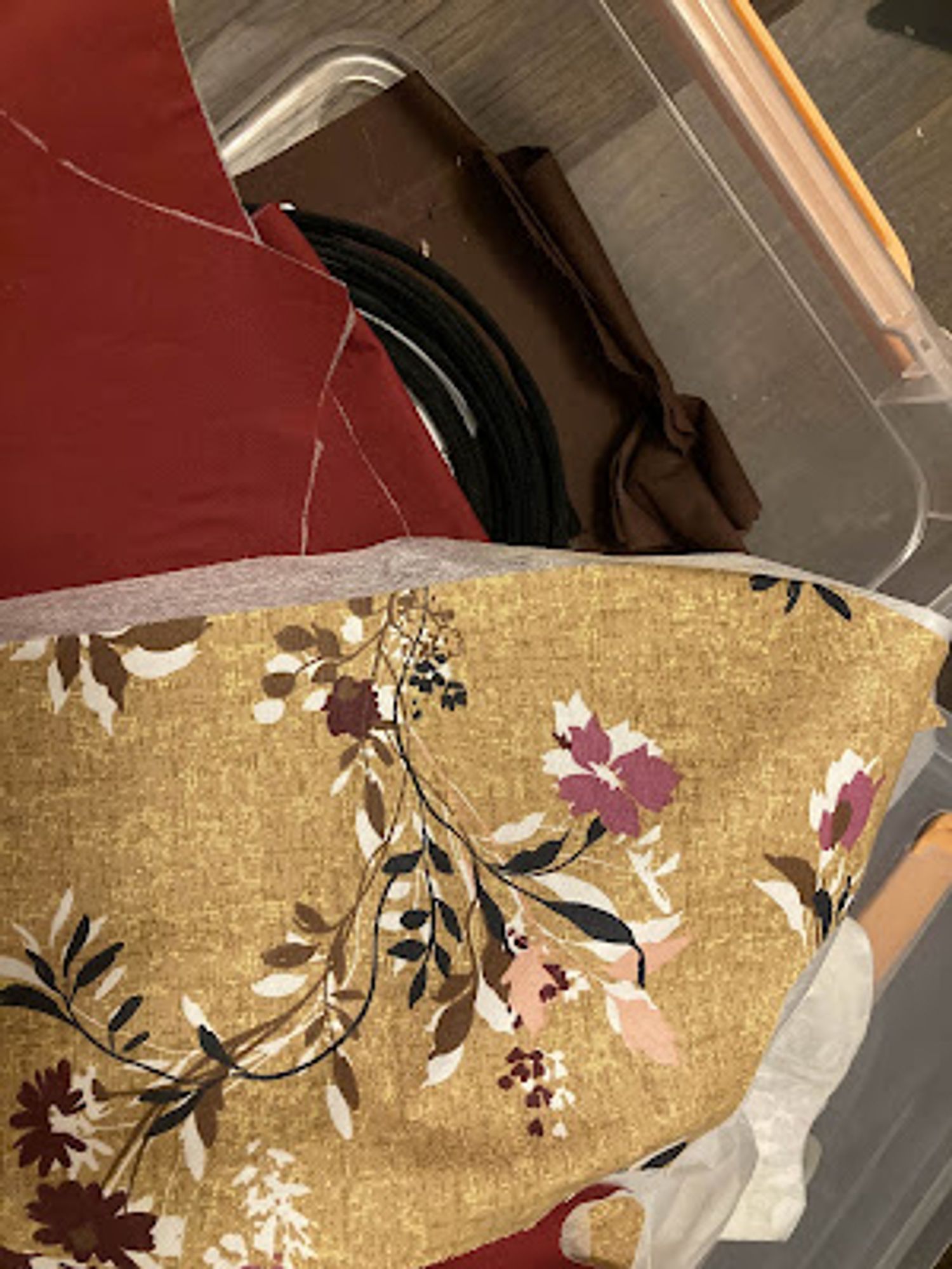 Pieces of fabric, cut into various shapes. The top one is a tan/yellow with red/brown/white flowers, below it is a red fabric and a dark brown fabric, matching the flowers in the yellow fabric.