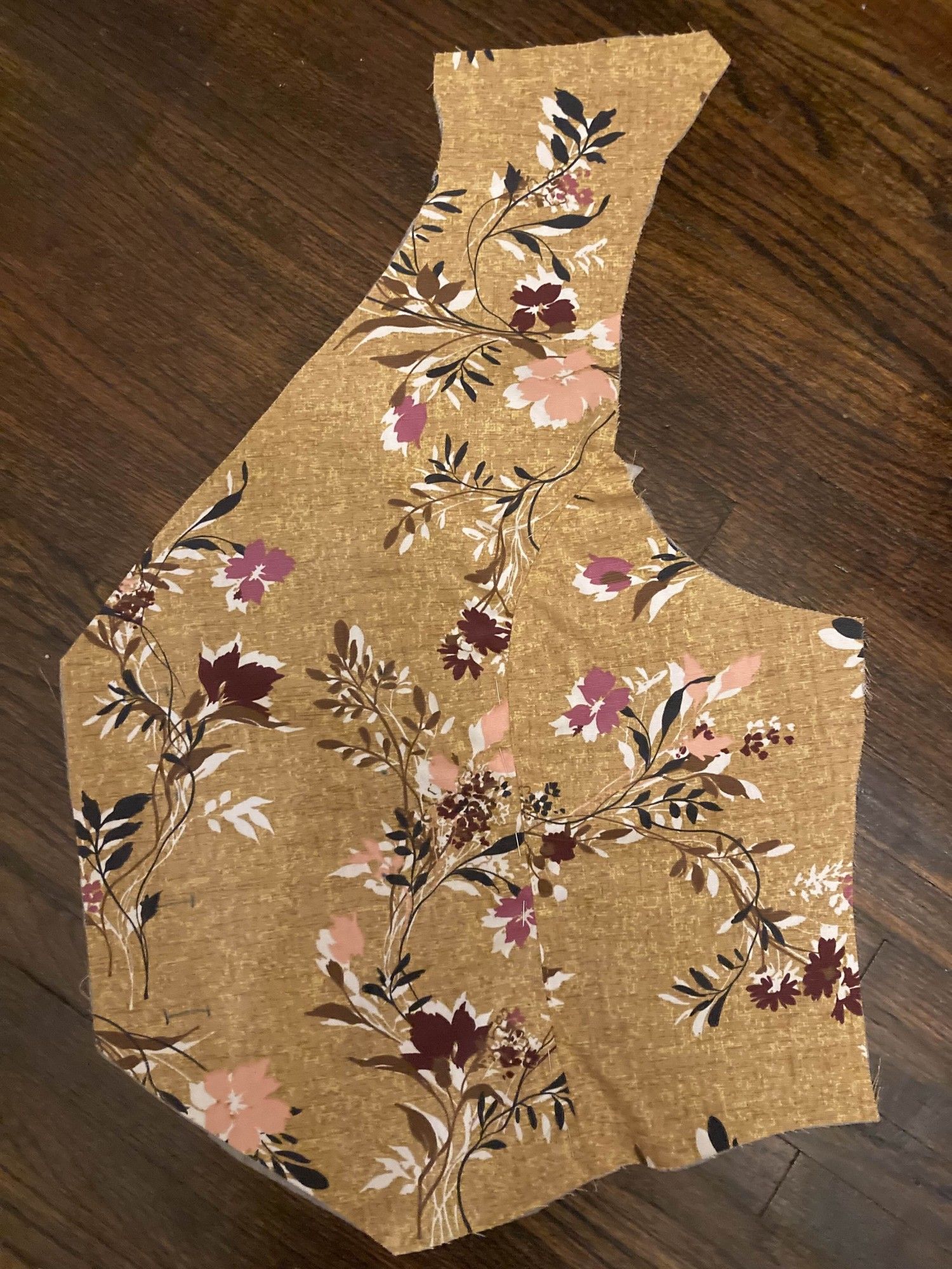 The front and side of the left half of a vest. The fabric is a mottled, golden brown with stylized flowers using layers of black, brown, white, peach, pink, and dark red.