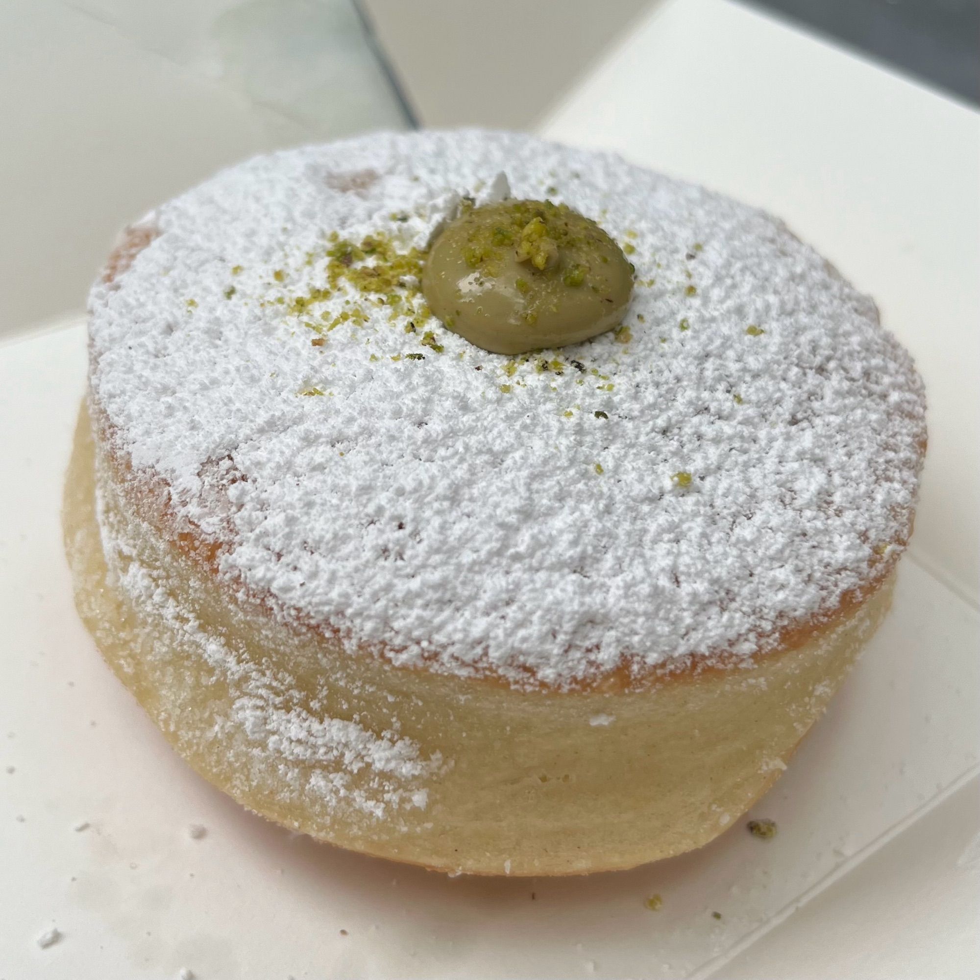 A heavily powdered donut —. no hole — with a dot of pistachio peeking out up top.