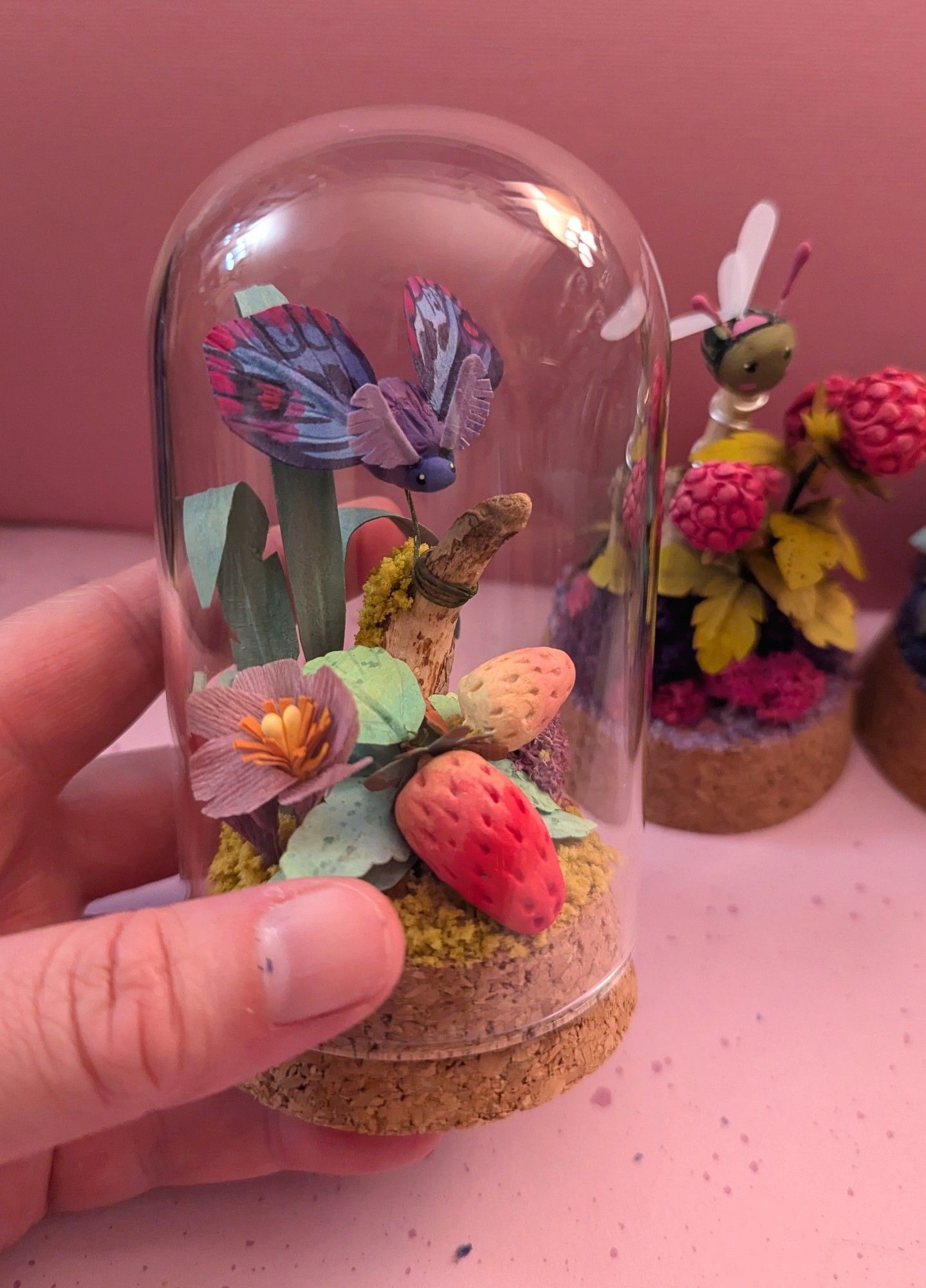 Sculpture with insect and strawberry on cork base with glass dome.