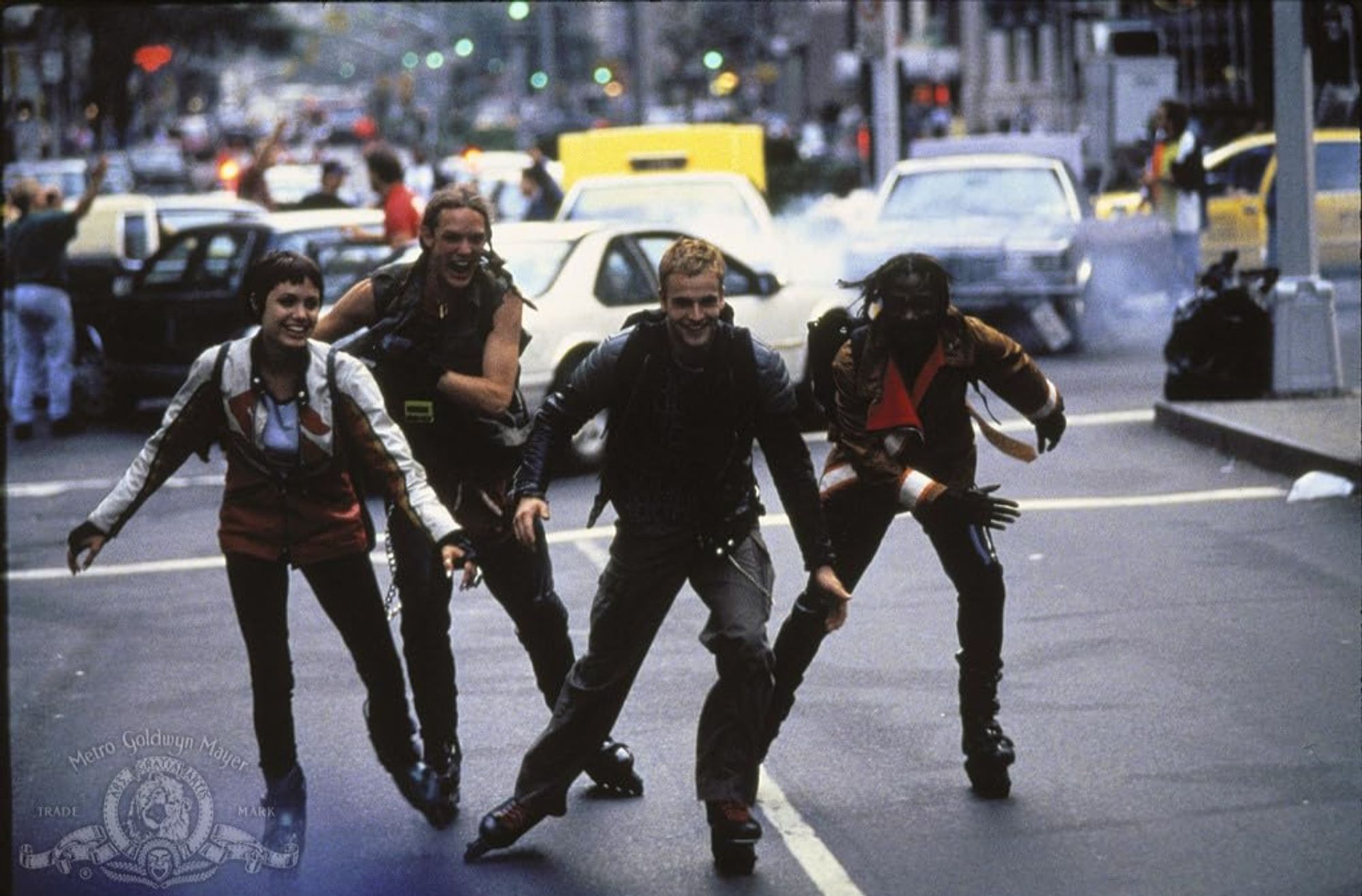 A production still from Hackers (1995) of four characters rollerblading in the streets of Manhattan. From left to right, it's Acid Burn (Angelina Jolie), Cereal Killer (Matthew Lillard), Crash Override (Jonny Lee Miller), and Lord Nikon (Laurence Mason).