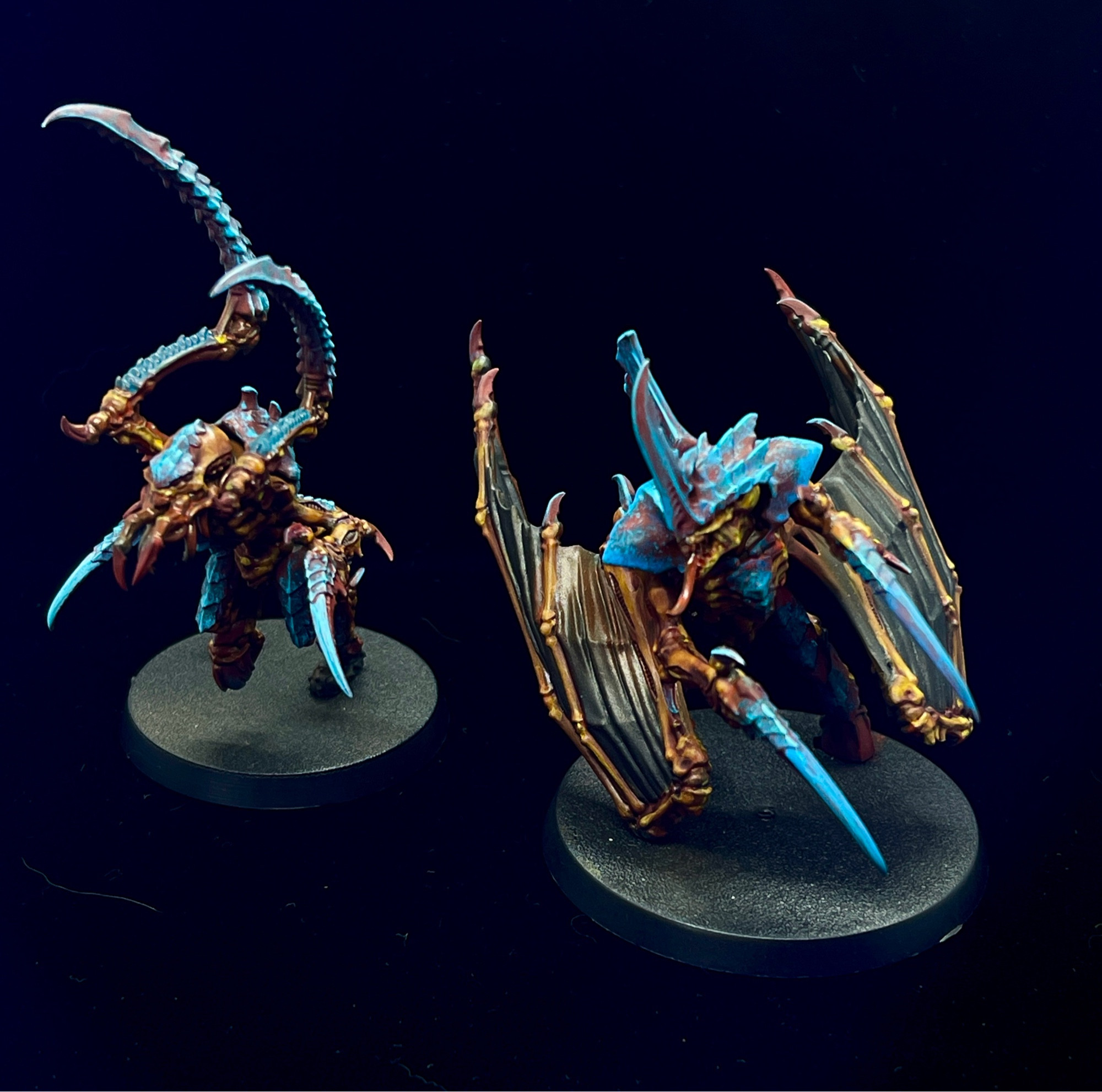 Two Tyranids from Warhammer 40K. The bug-like creatures feature bright blue claws and blades with a red carapace and orange/yellow skin