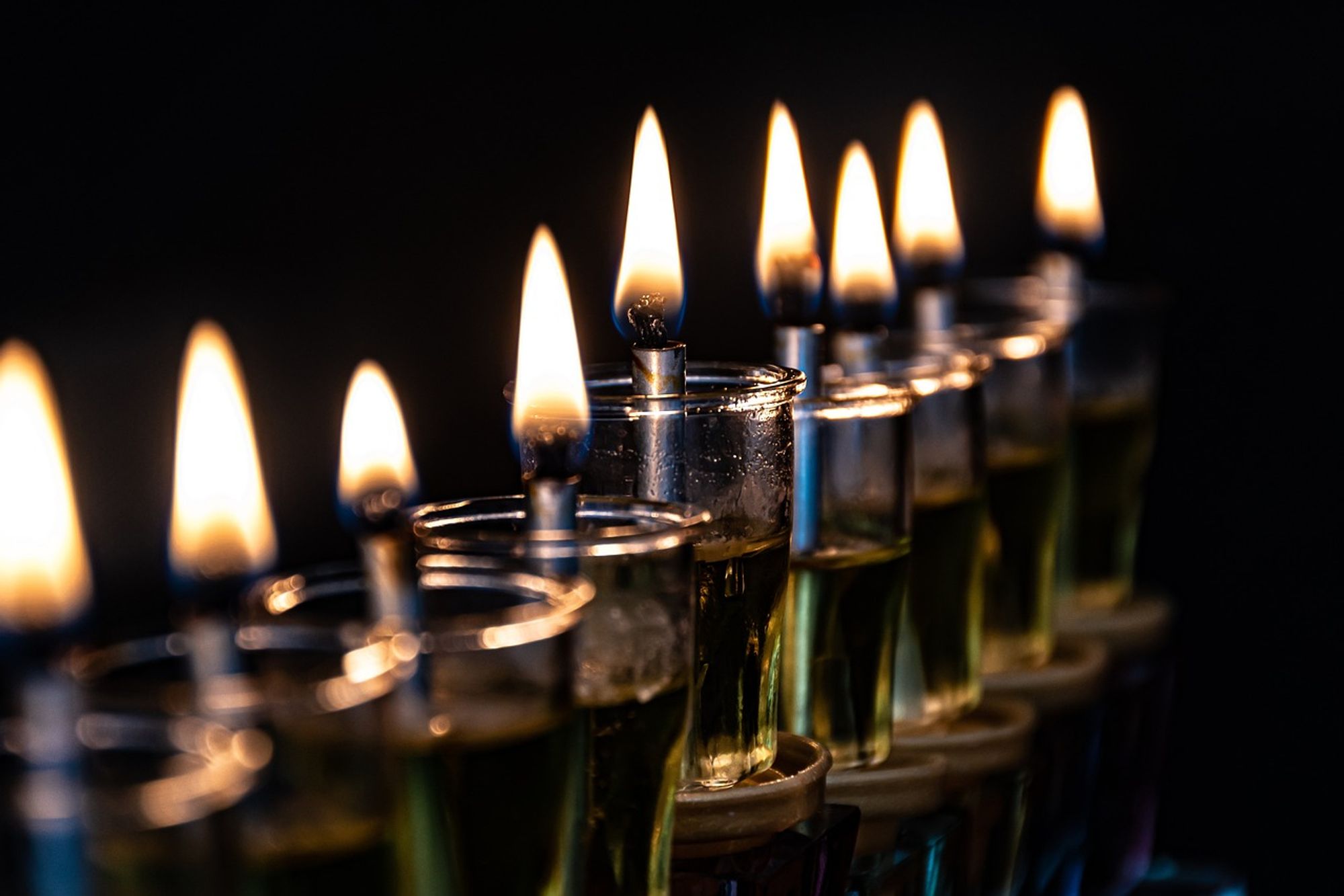 9 wicks burn in individual glass oil lamps on a menorah, courtesy Ri_Ya via Pixabay