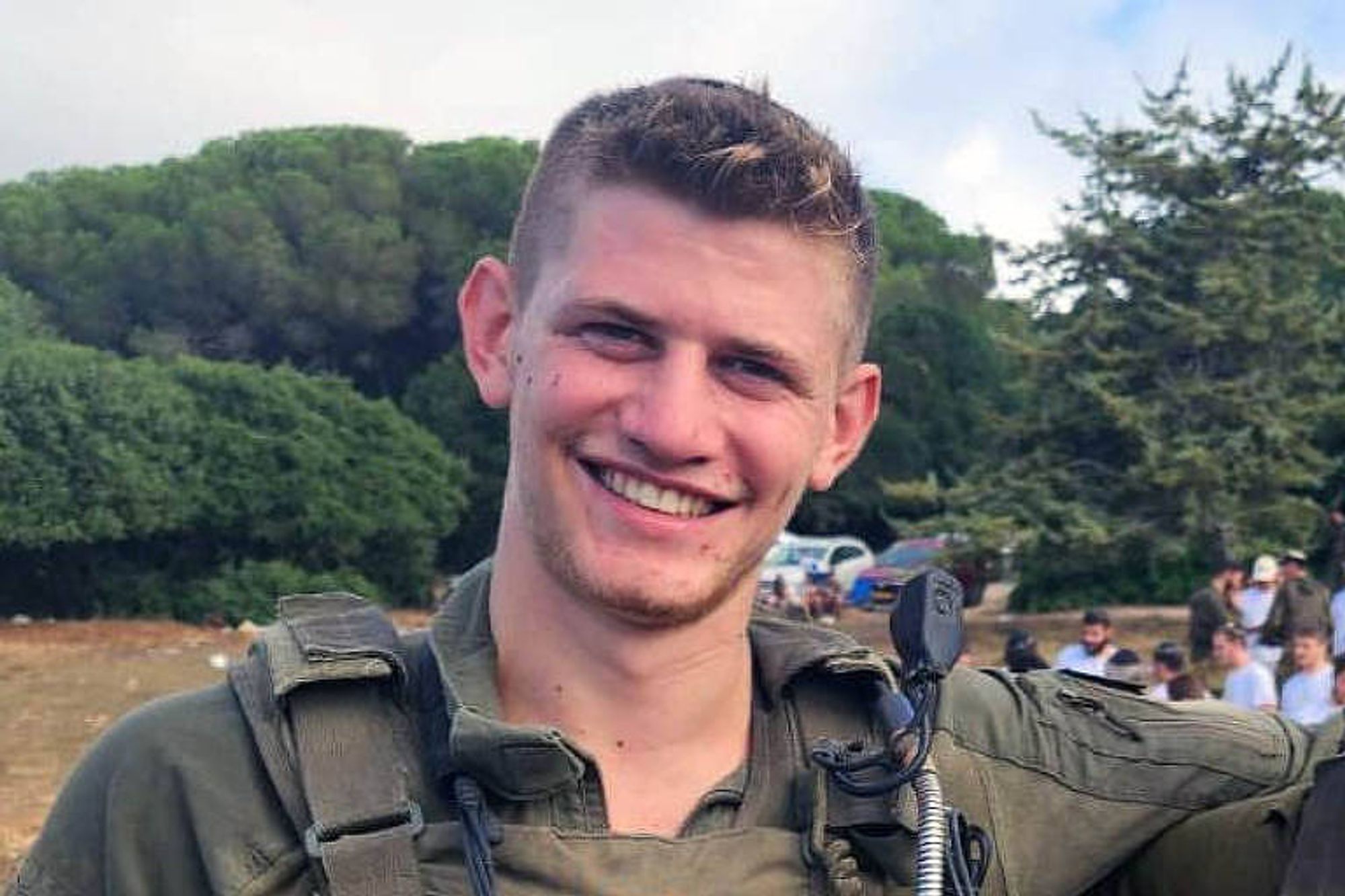 Fotografia colorida é retrato de soldado israelense, fardado. Ele é um homem branco, loiro, de cabelos lisos e curtos, e está sorrindo.