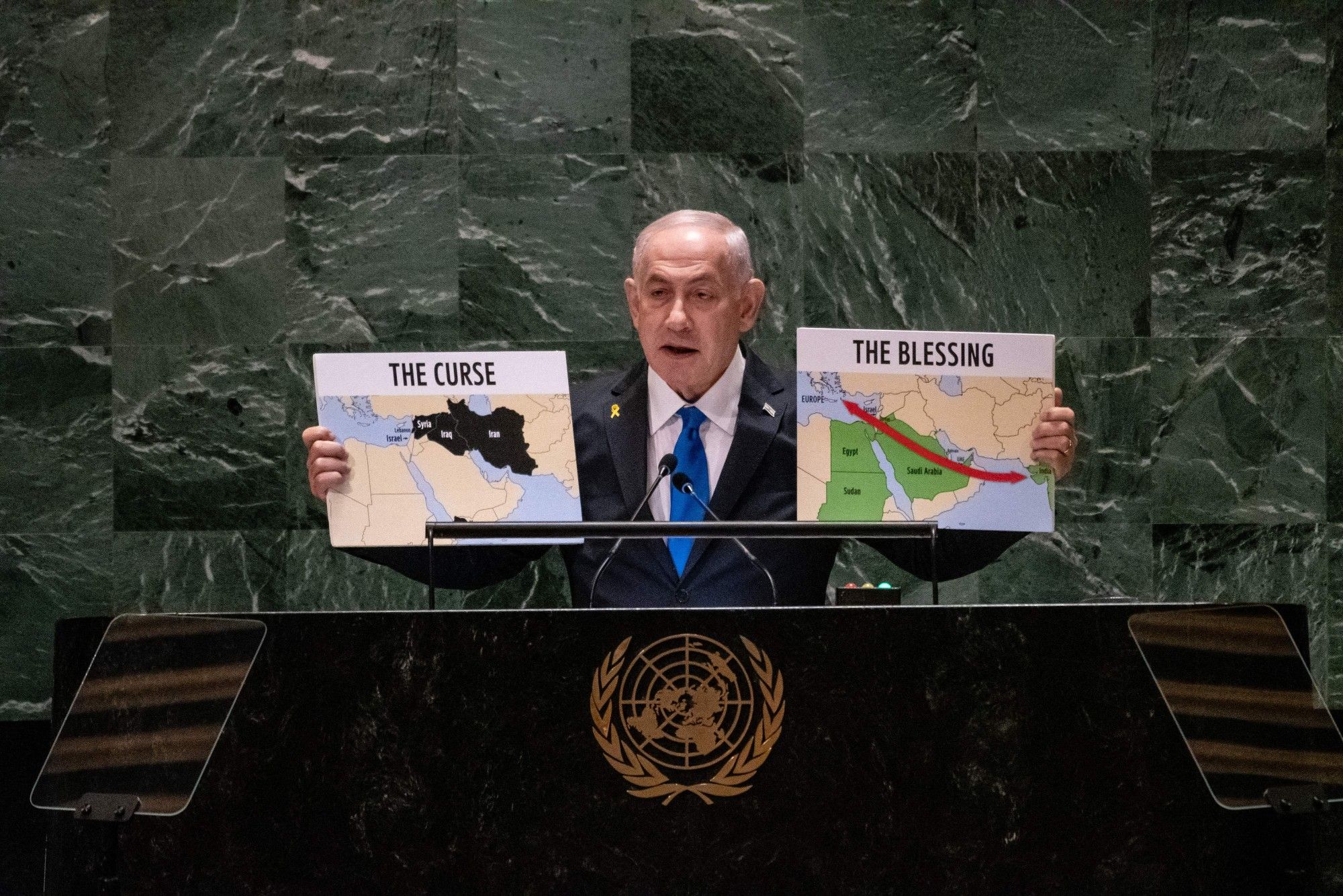 Fotografia colorida mostra Netanyahu discursando durante Assembleia da ONU. Com a mão direita ele mostra um mapa do Oriente Médio com o título "A Maldição" e, com a esquerda, um outro mapa, também do Oriente Médio, com o título "A Benção"