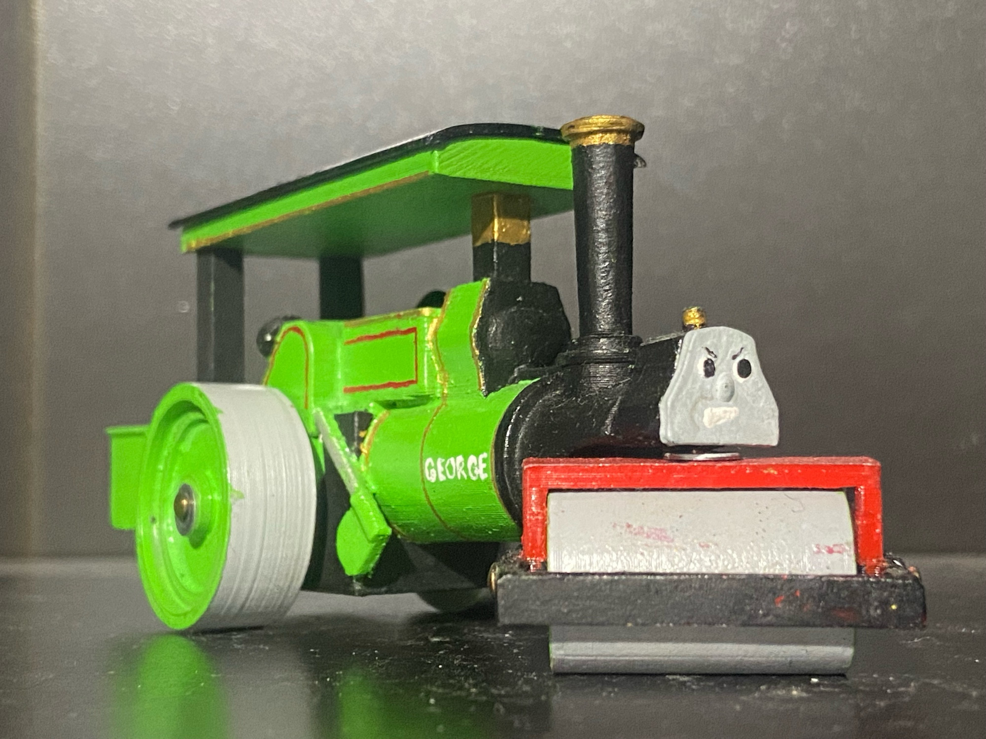 Side profile of George.

His name is written on his boiler in white capital letters: GEORGE.

His roller has a red and black holder piece 

He has red stripes and gold stripes.

He’s also really angry. Probably because you HAVEN’T RIPPED UP THE RAILS AND TURNED THEM INTO ROADS.