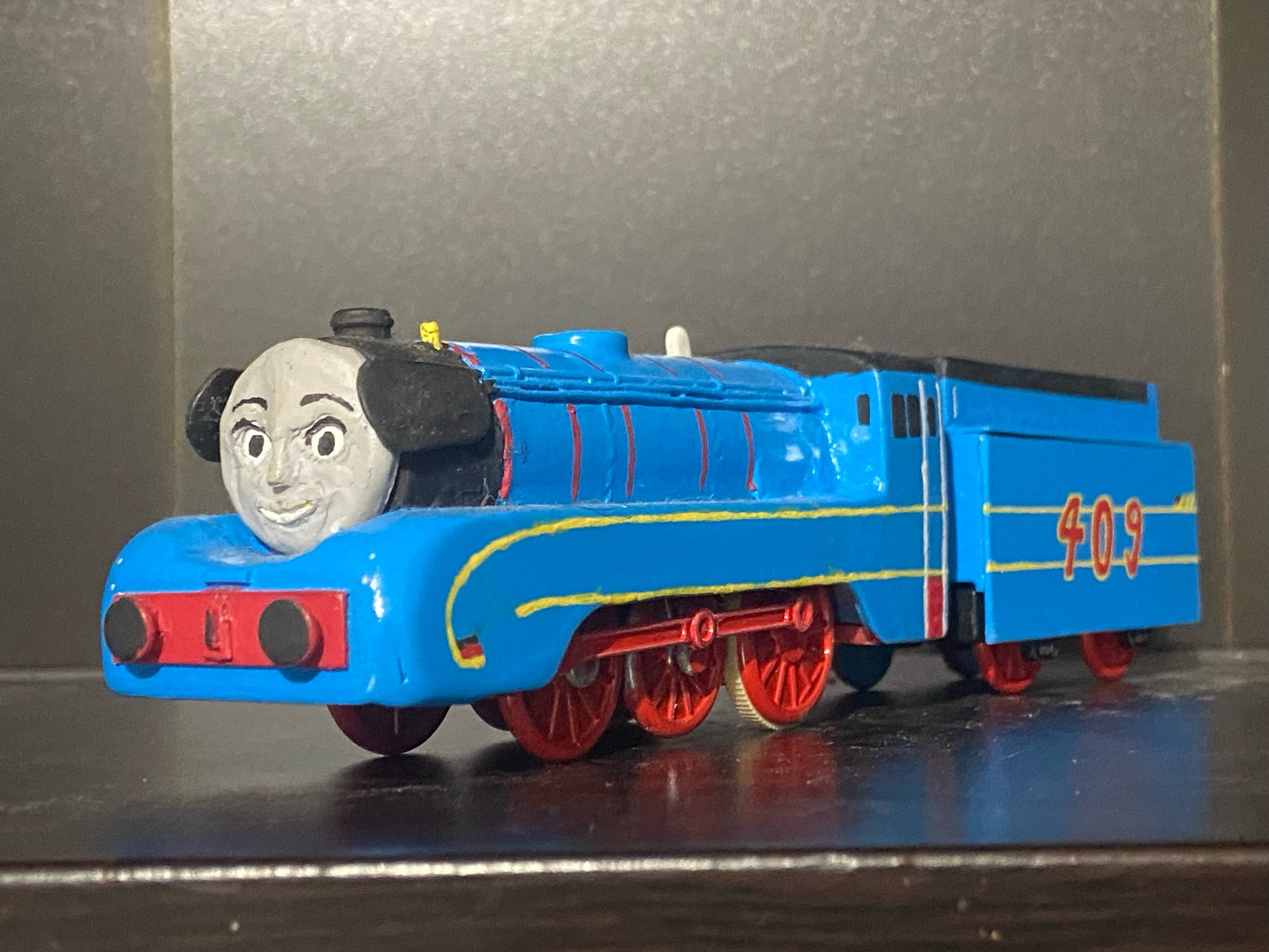 Side profile of Frieda.

She is painted blue, has red wheels and rods, has yellow lining with the German flag at each end of the top yellow stripe, a black roof, and 409 written in red with a yellow outline.