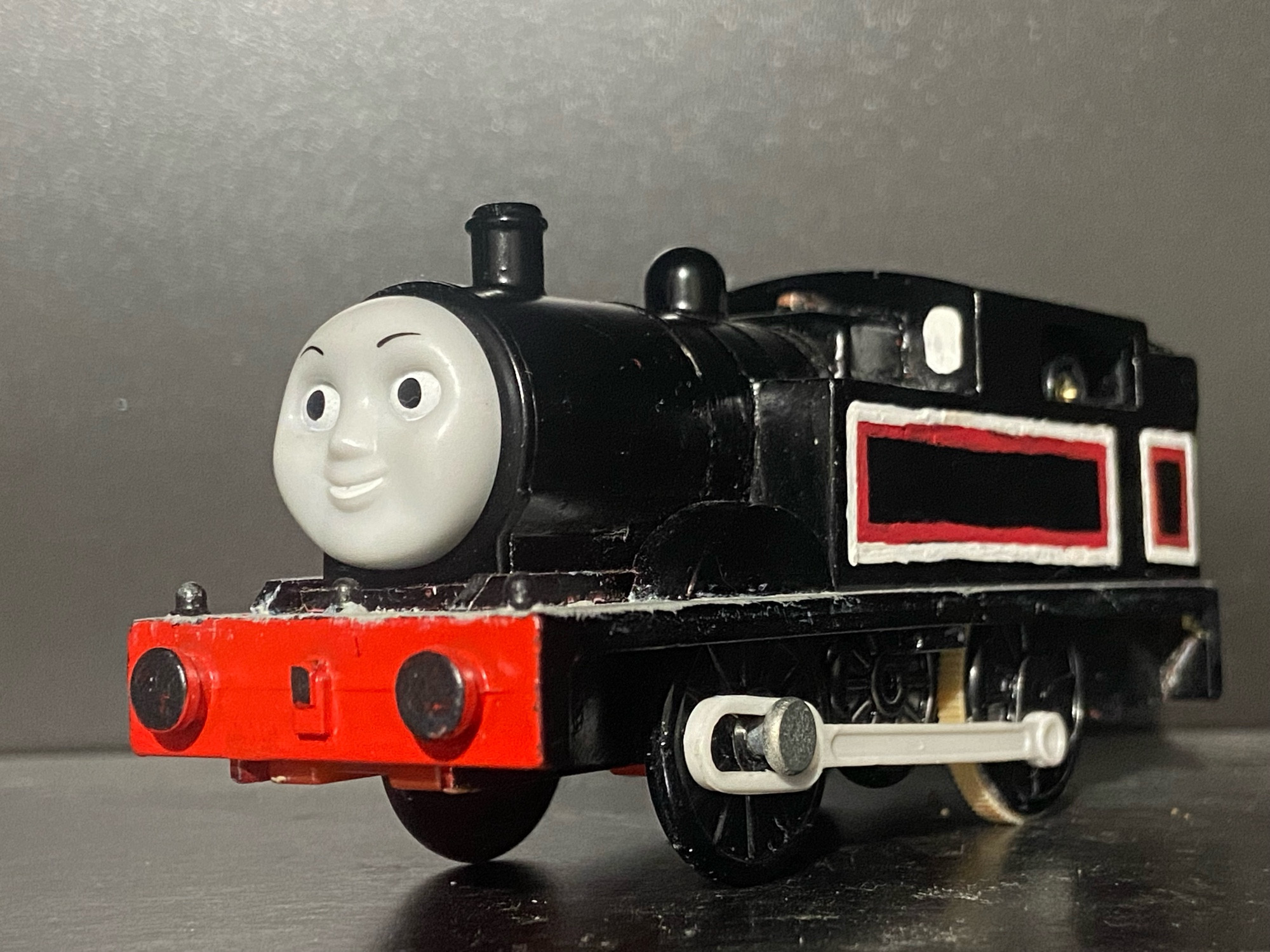 Side profile of Jinty, she has two tone white and red stripes across her side tanks, cab, and bunker. There are white portholes on the front of her cab and she has a light grey footplate.