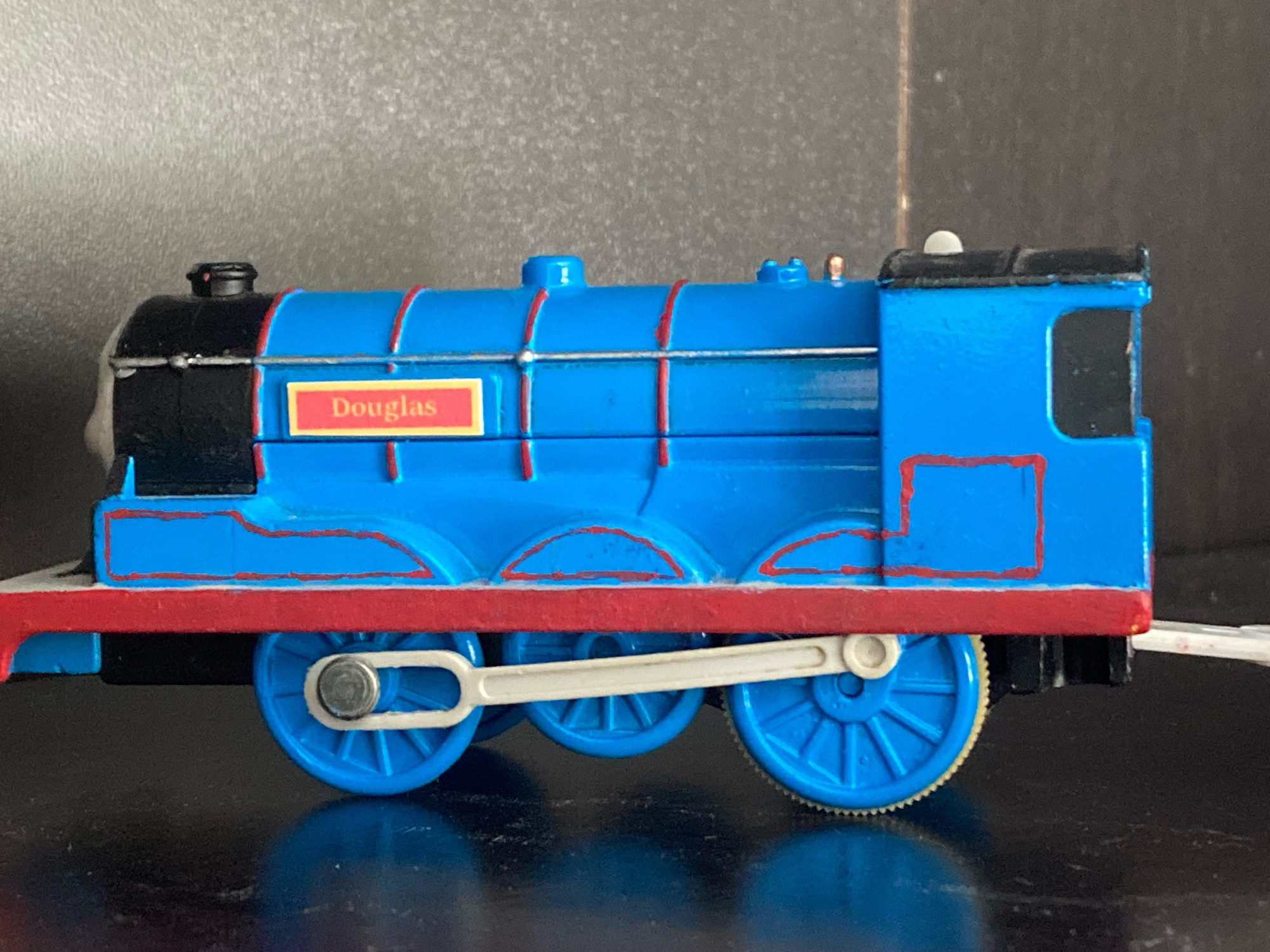 Side profile of Douglas, his blue paint is fully visible alongside his red stripes. His nameplate is yellow and red and reads “Douglas” in yellow text.