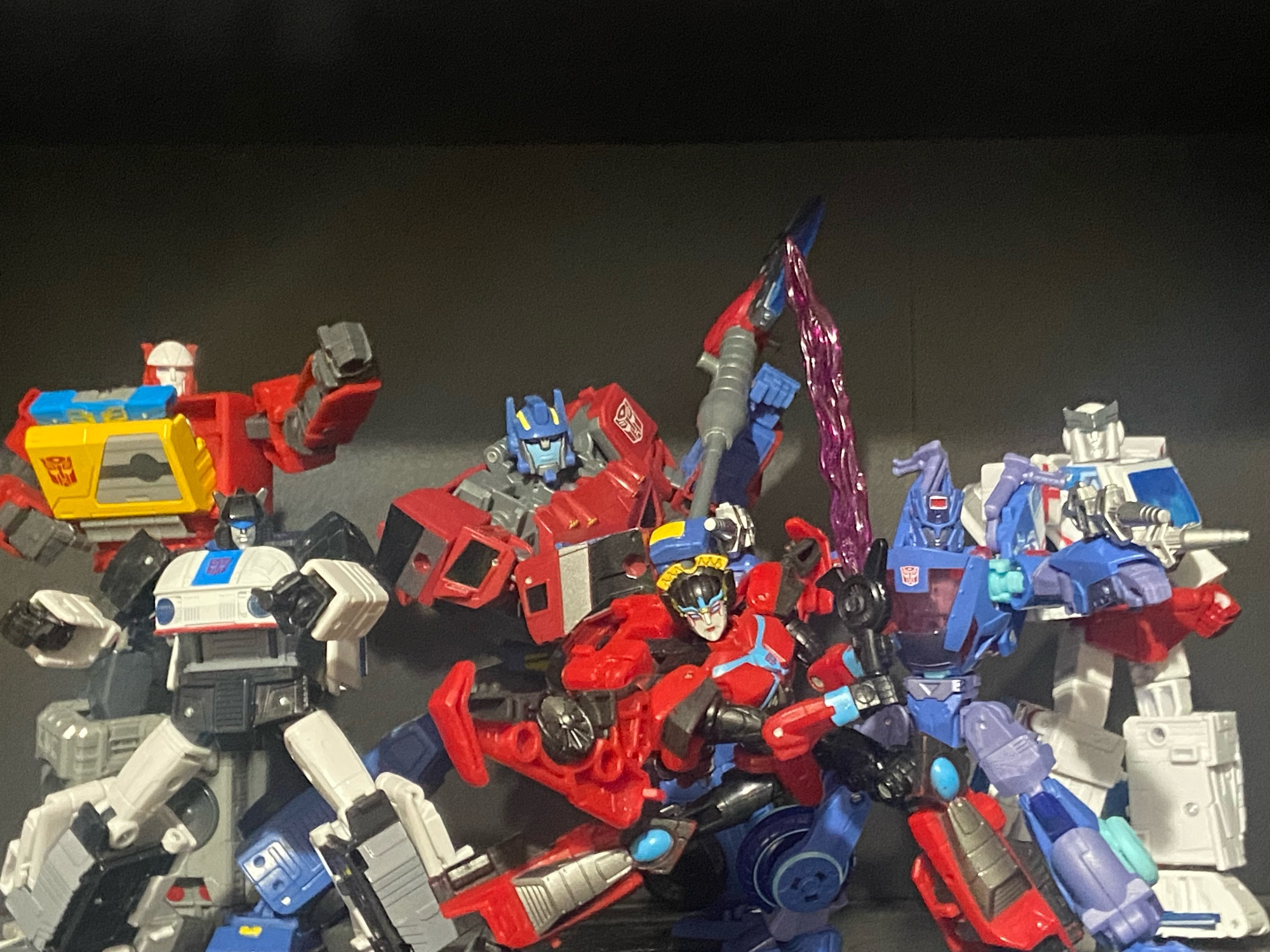 A photo of six autobots from various incarnations of the Transformers franchise.

From left to right the autobots in the photo are Generation 1 Blaster, Generation 1 Jazz, Animated Optimus Prime, Cyberverse Windblade, Cyberverse Chromia, and Generation 1 Ratchet.