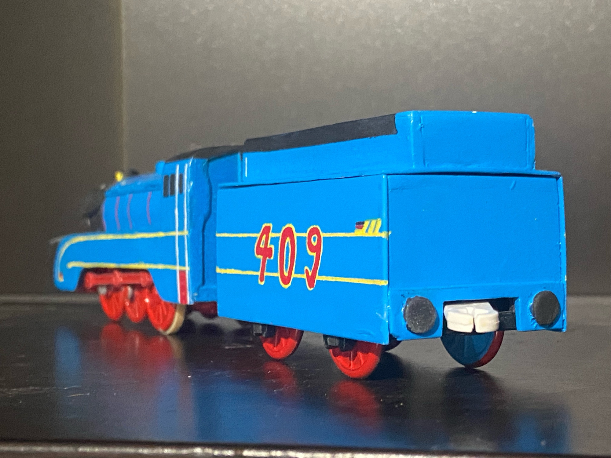 Rear profile of Frieda.

She is painted blue, has red wheels and rods, has yellow lining with the German flag at each end of the top yellow stripe, a black roof, and 409 written in red with a yellow outline.