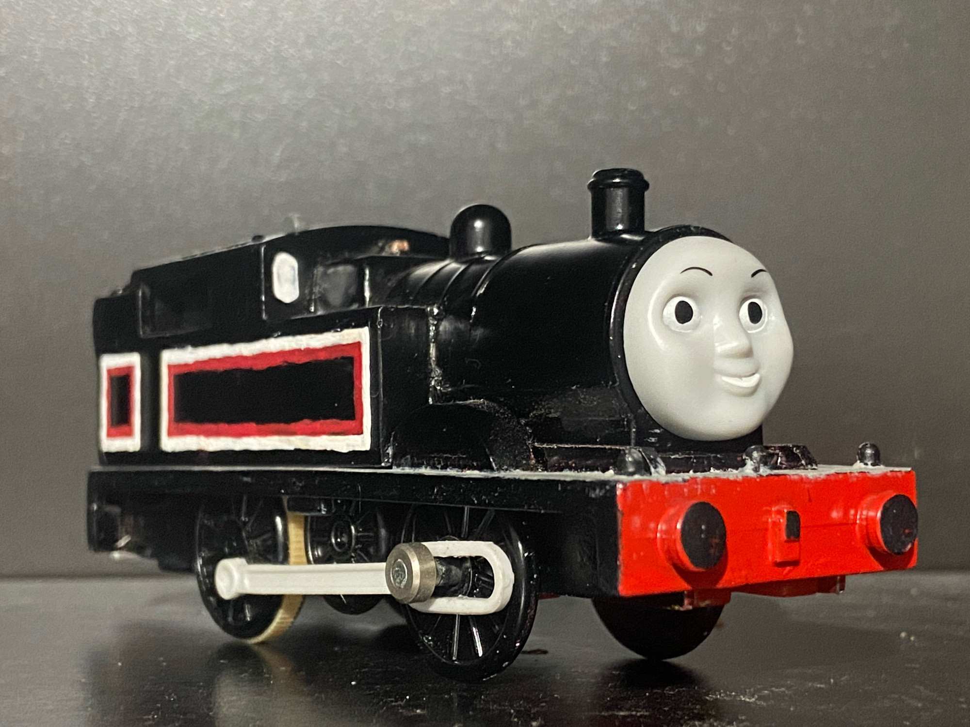 Side profile of Jinty, she has two tone white and red stripes across her side tanks, cab, and bunker. There are white portholes on the front of her cab and she has a light grey footplate.