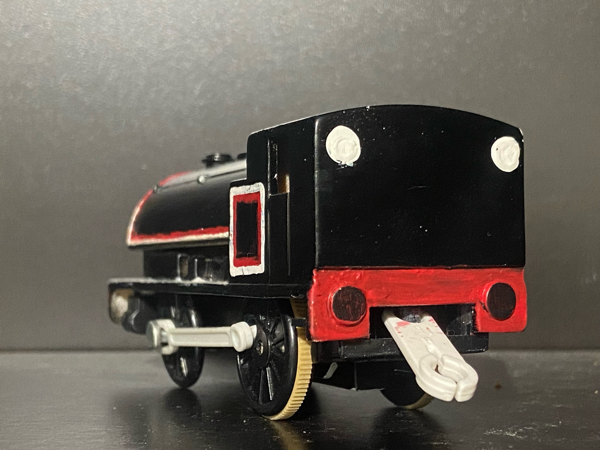 Side profile of Jinty, she has two tone white and red stripes across her saddle tank and bunker. There are white portholes on the rear of her cab and she has a light grey footplate.