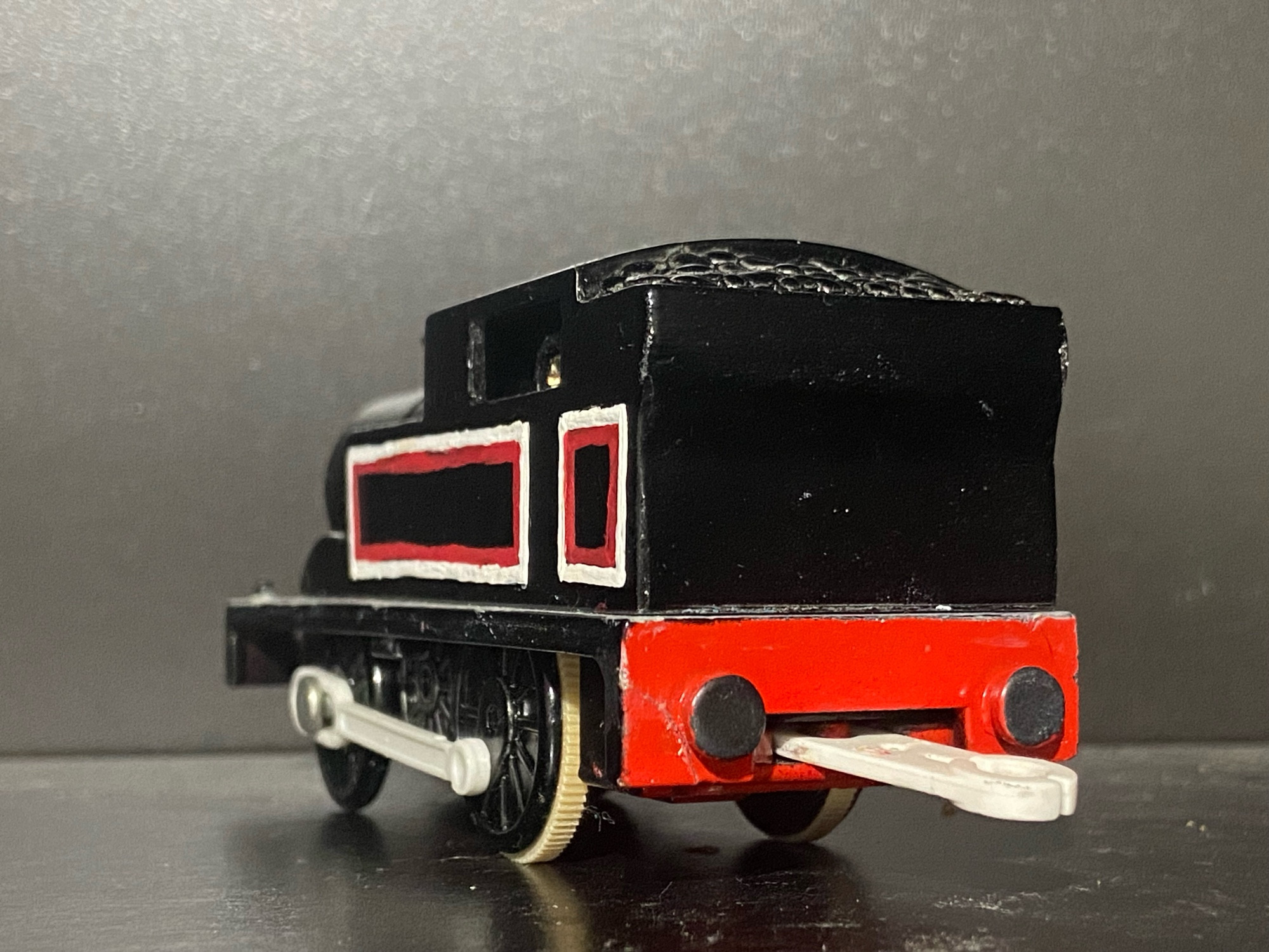 Rear profile of Jinty, she has two tone white and red stripes across her side tanks, cab, and bunker. There are white portholes on the front of her cab and she has a light grey footplate.