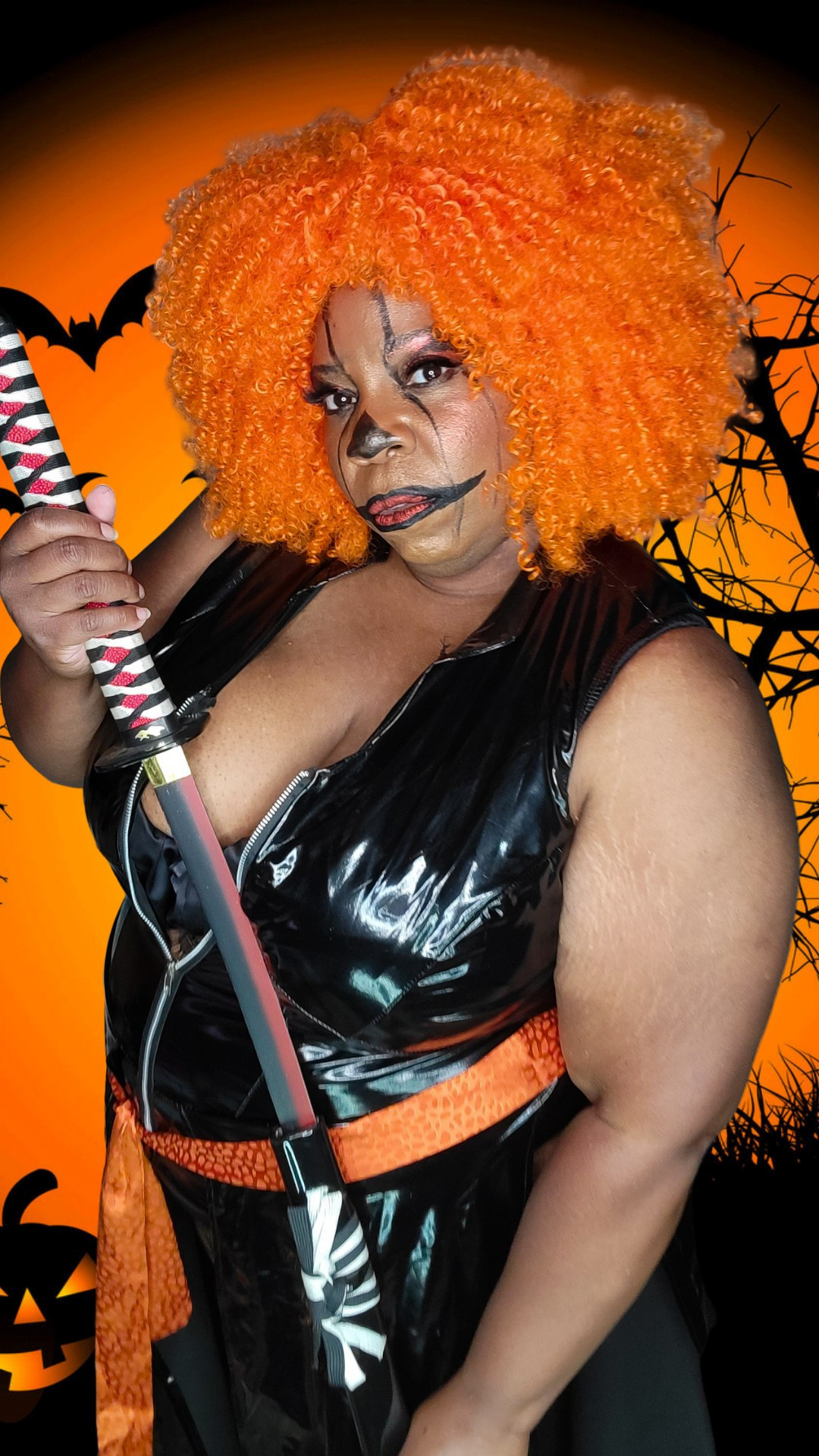 TaLynn Kel with curly orange hair, pumpkin makeup, wearing a vinyl dress holding a katana.