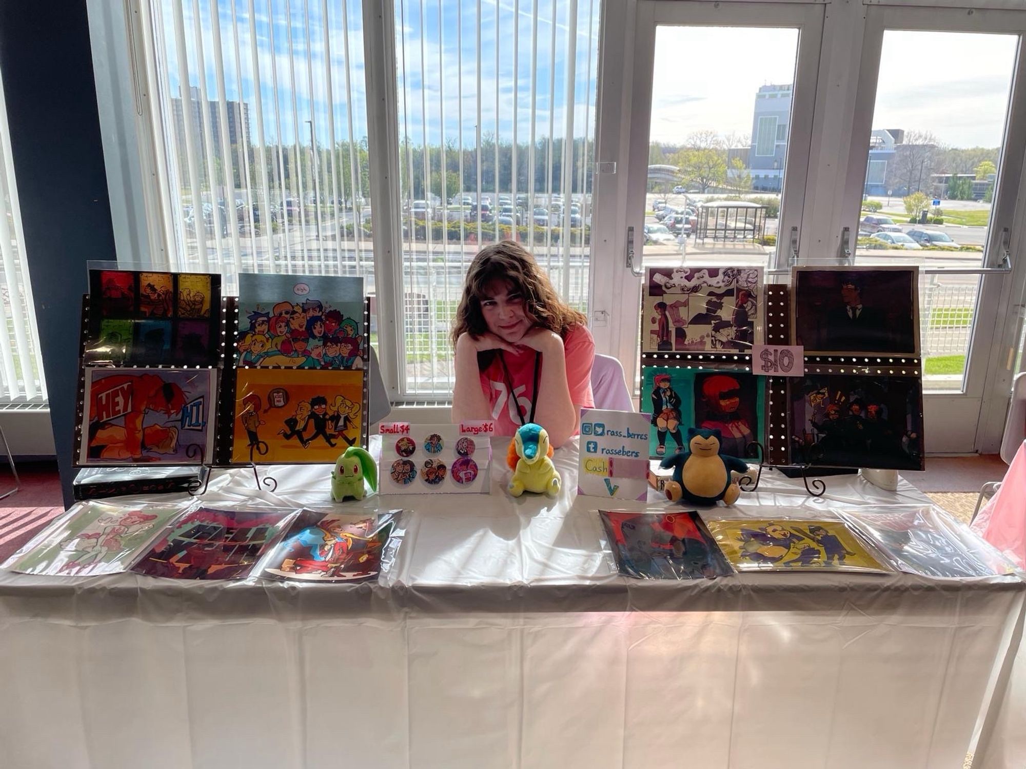 Display of art prints and art buttons for sale on a table at a con. Prints are of various anime characters.