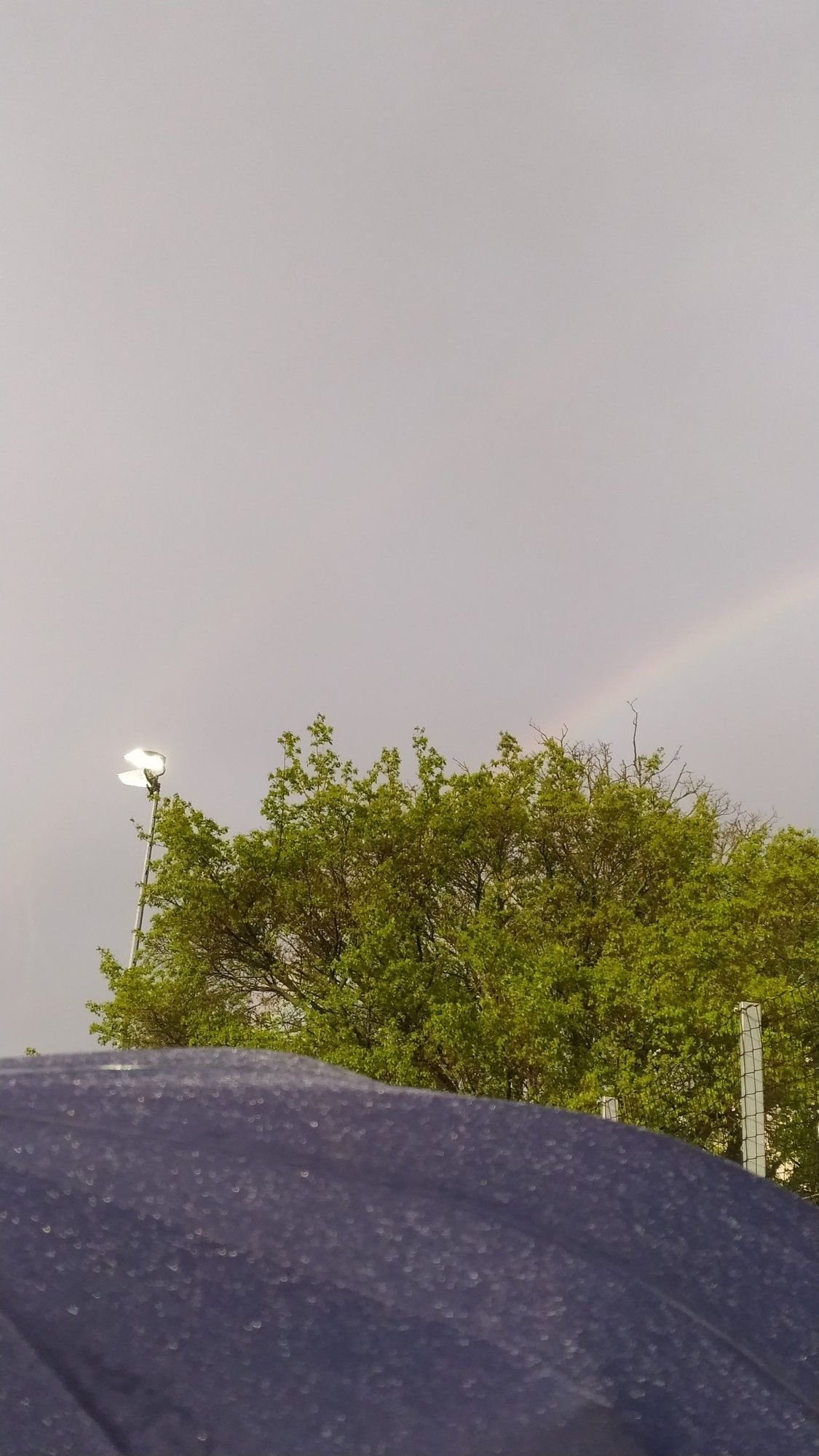 Regenbogen neben einem Flutlichtmast