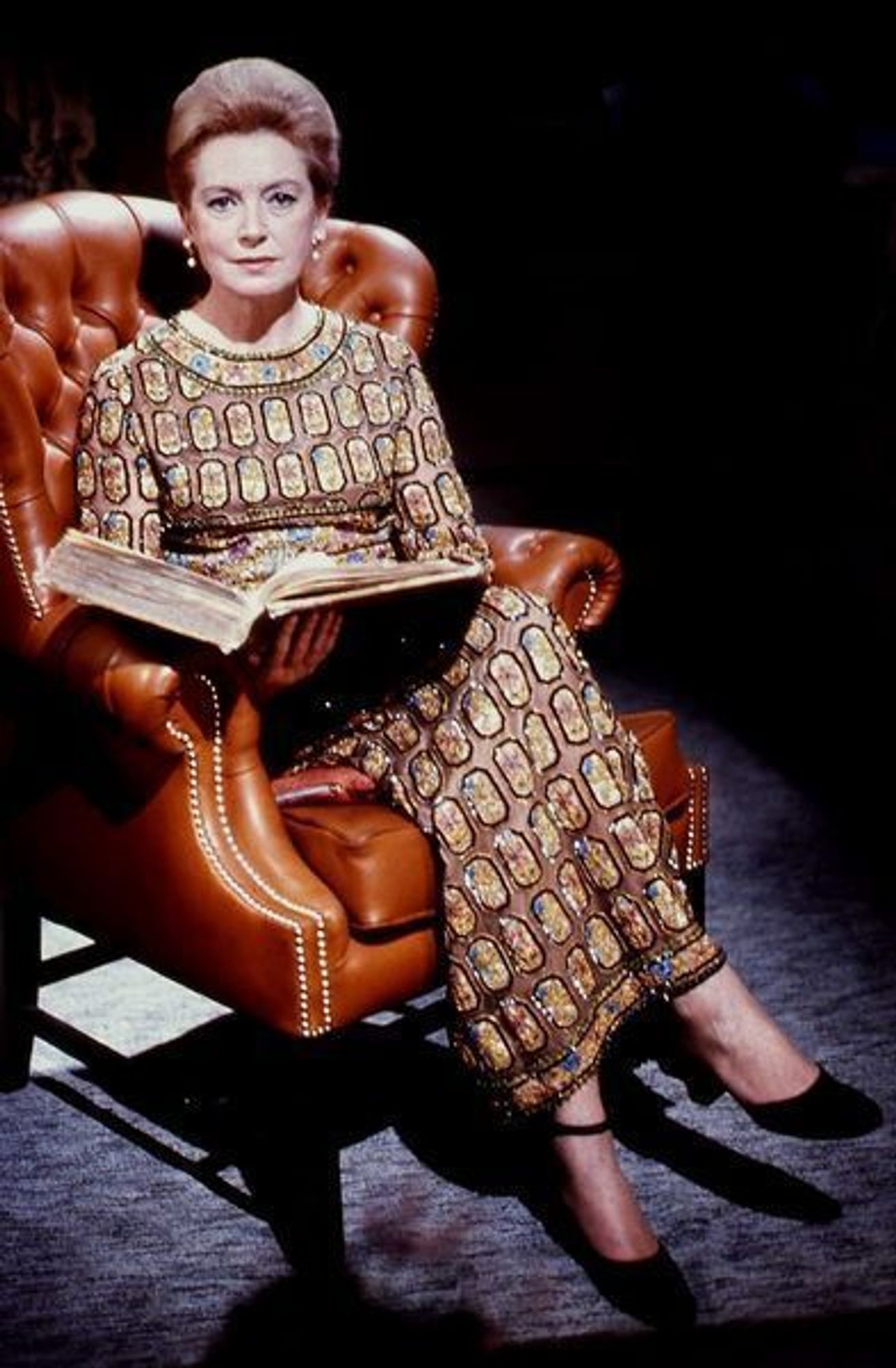 Photo de Deborah Kerr, assise dans un fauteuil rouge, un livre ouvert dans les mains