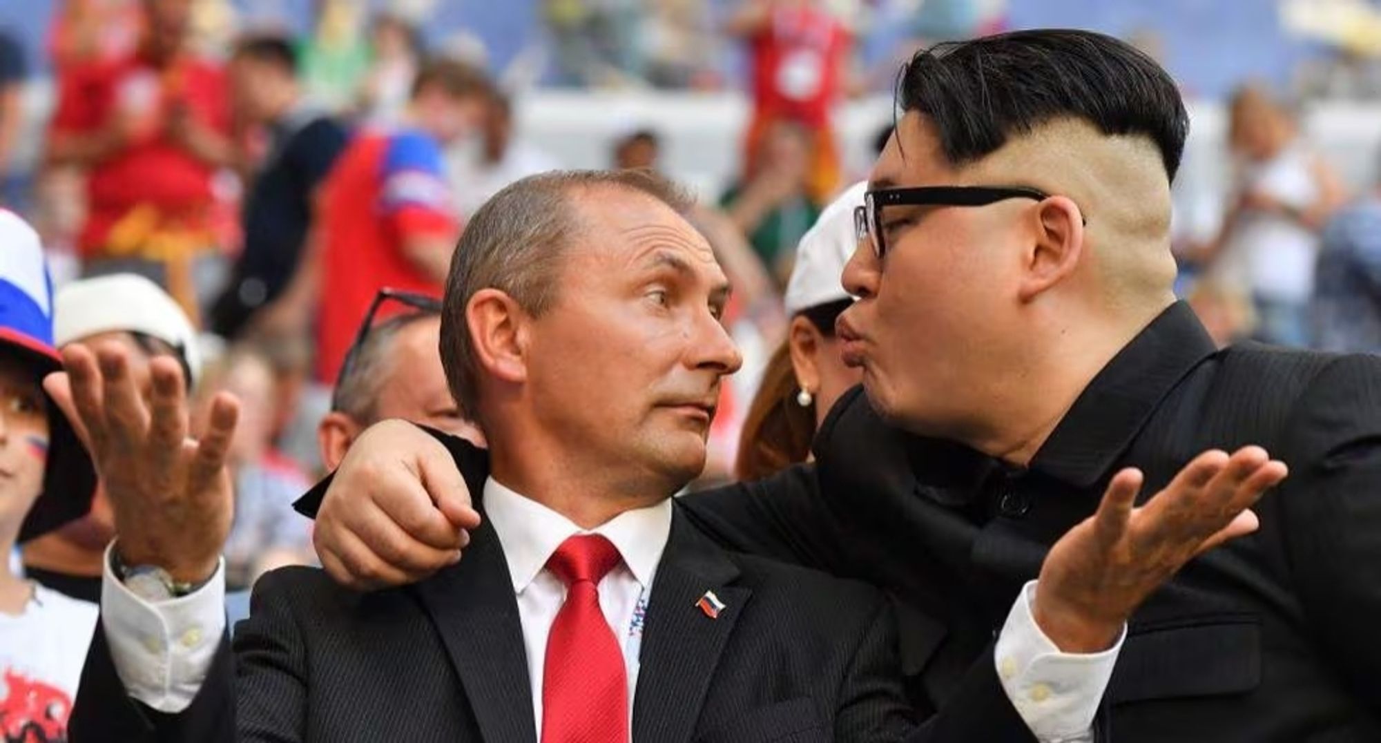 Foto Querformat 
Putin und Kim Jong-un küssen sich auf einer Großveranstaltung bei der im Hintergrund verschwommen viele Menschen zu sehen sind.