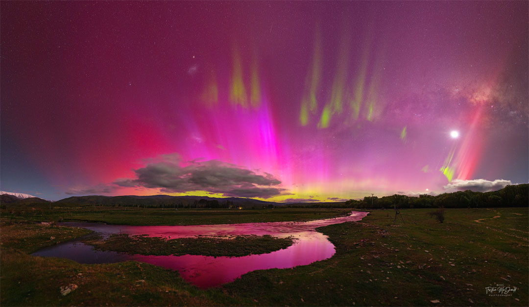 Sometimes the night sky is full of surprises. Take the sky over Lindis Pass, South Island, New Zealand one-night last week. Instead of a typically calm night sky filled with constant stars, a busy and dynamic night sky appeared. Suddenly visible were pervasive red aurora, green picket-fence aurora, a red SAR arc, a STEVE, a meteor, and the Moon. These outshone the center of our Milky Way Galaxy and both of its two satellite galaxies: the LMC and SMC. All of these were captured together on 28 exposures in five minutes, from which this panorama was composed. 