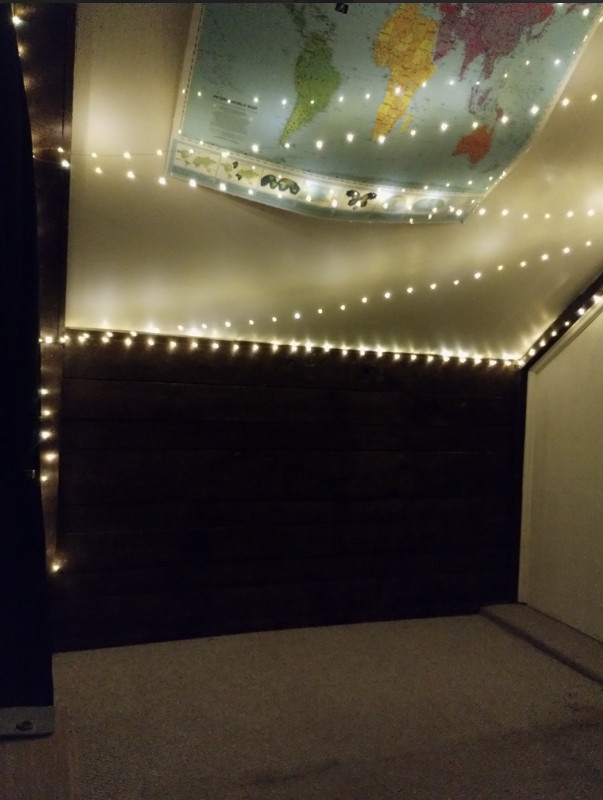 a low dark brown wall with fairy lights strung across a ceiling that at a 45 degree angle overhead. a white faux wood paneled wall to the right