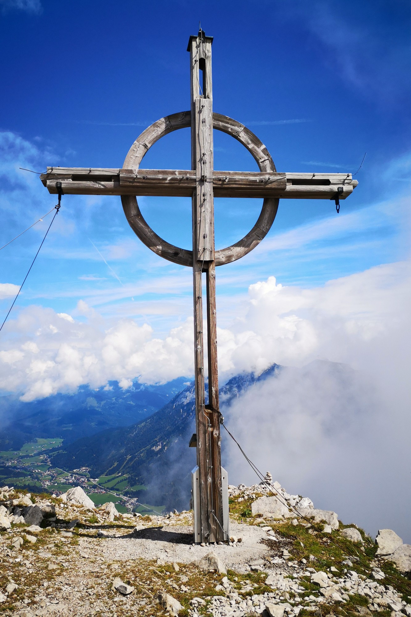 Großes Holzkreuz auf dem Gipfel der Seekarspitze (Vorkarwendel, Österreich). Der Himmel ist blau. Aus dem Tal ziehen weiße Wolken auf.