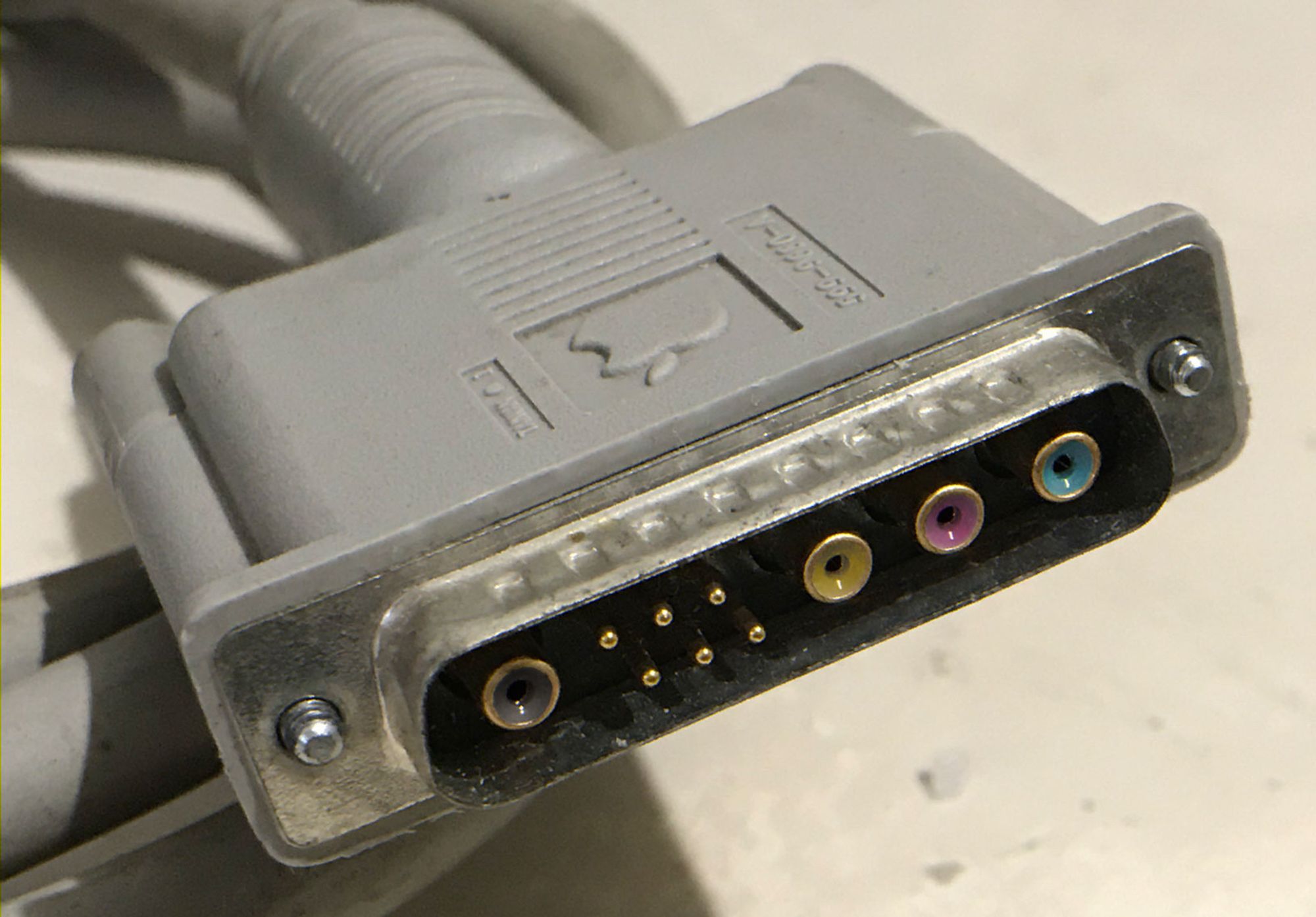 A photo of a 10W4 connector on the end of an Apple cable, with the four mini coax connectors coloured dark grey, yellow, magenta and cyan to enable the carriage of all CMYK colour data natively.