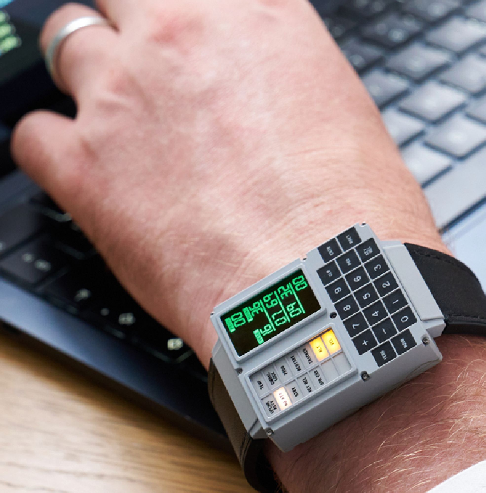 A photo of a wristwatch on the wrist of someone using a laptop. It looks just like a miniature apollo guidance computer, but fits on a wrist - but only just. It's still pretty chunkers which is part of the appeal.