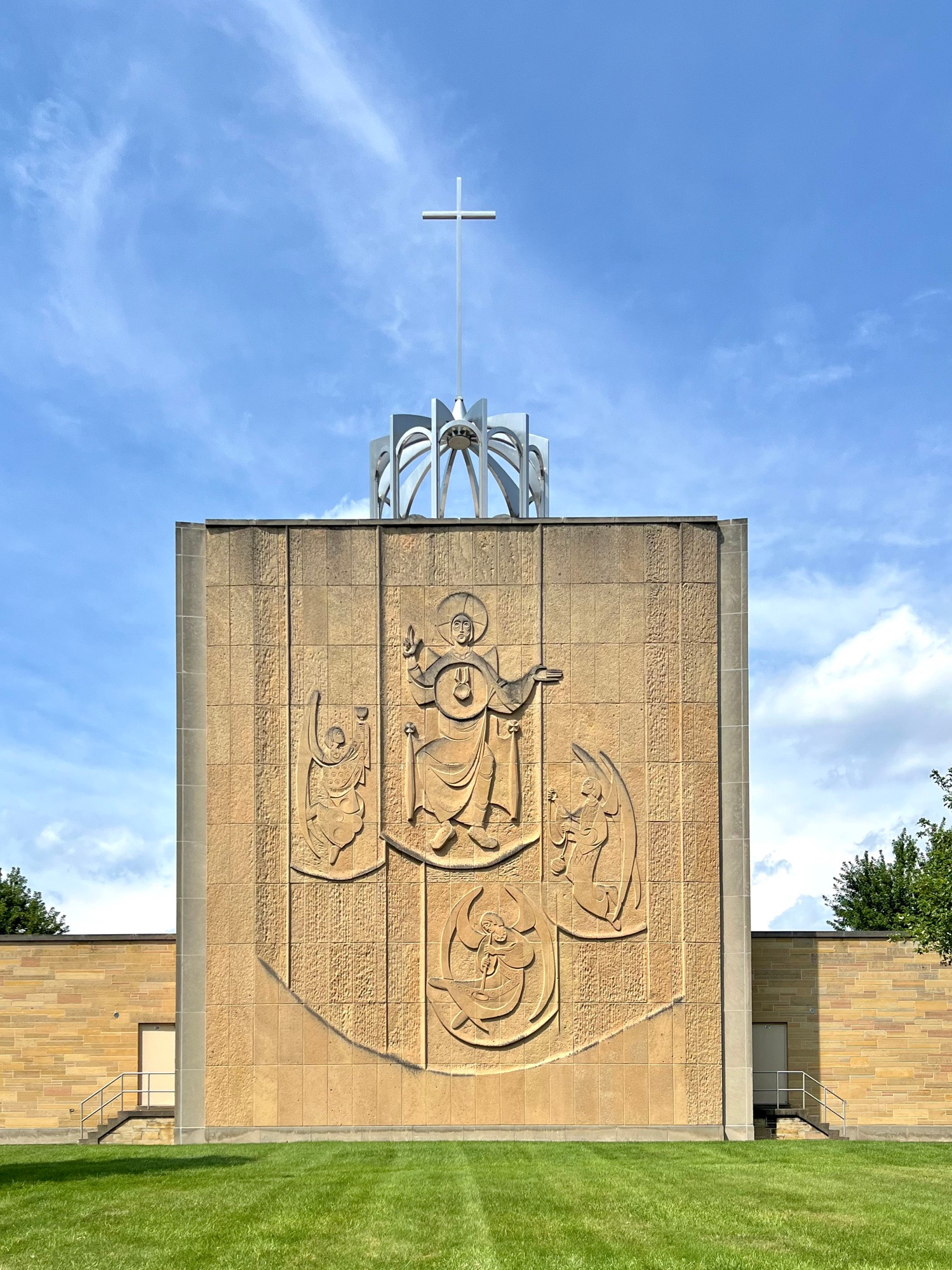 Large modernist religious relief of four figures on a stone wall with a cross structure above.