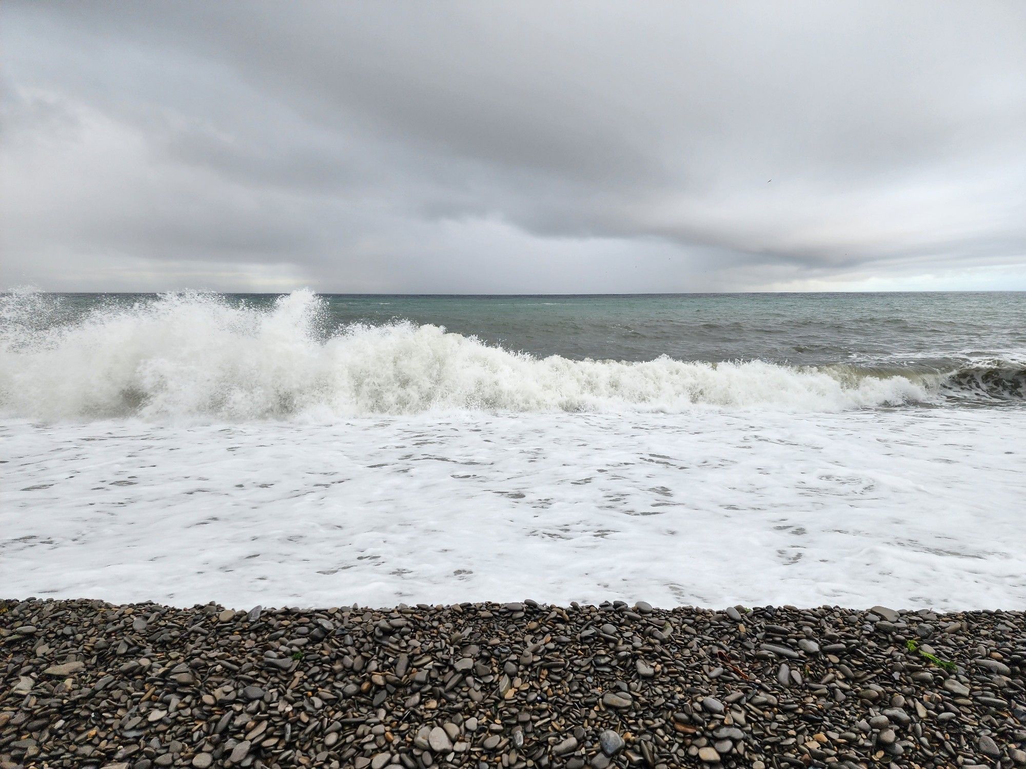 A pebble beach with ocean waves and cloudy skies