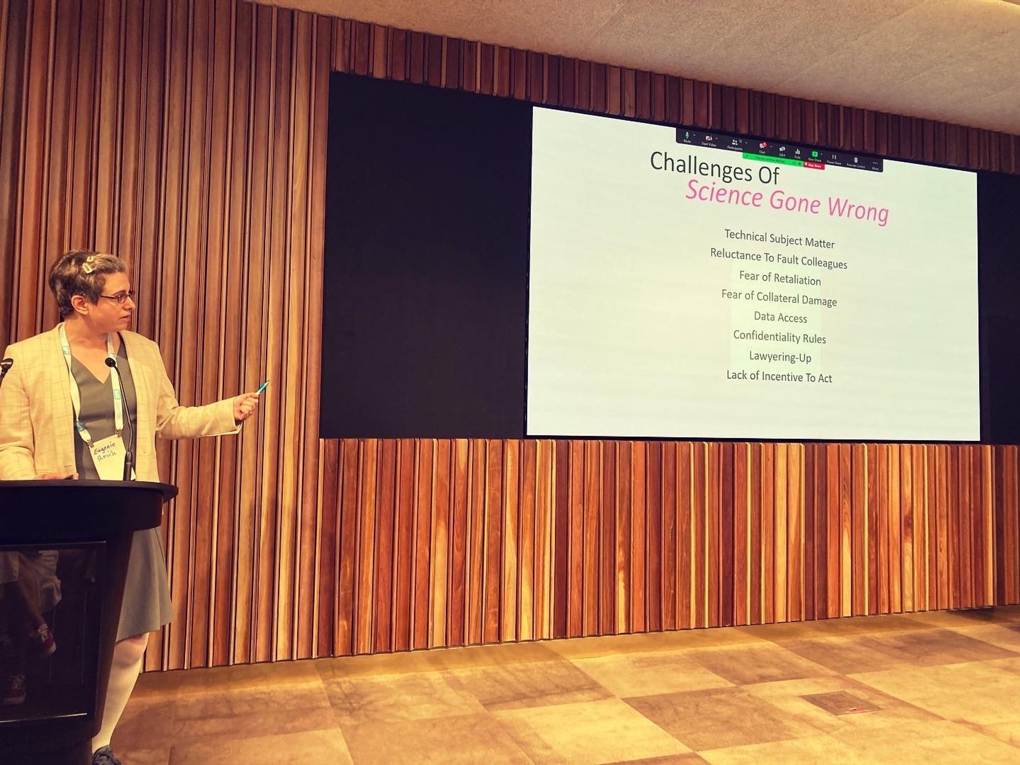 Eugenie Reich delivering a talk at a podium, with a screen of her presentation next to her