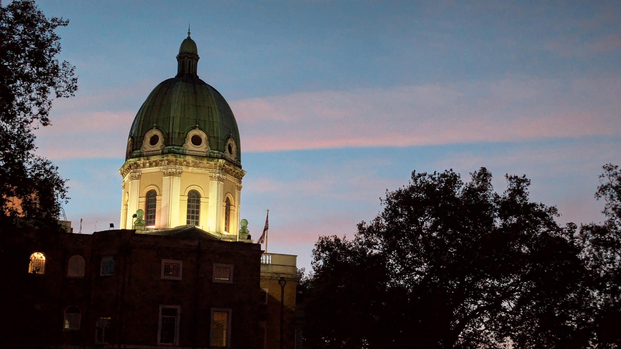 Domed building against a twilit sky with a broad band of straight pink cloud apparently projected by the dome