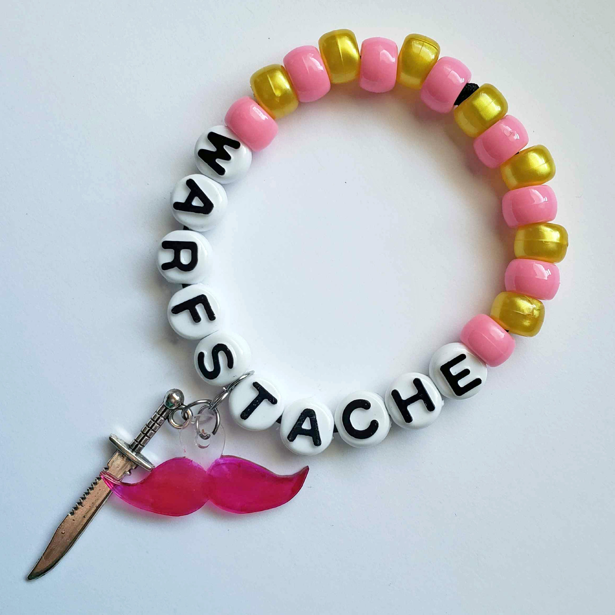 A pink and yellow bracelet that reads "Warfstache;" from it hangs a pink mustache charm and a knife charm.