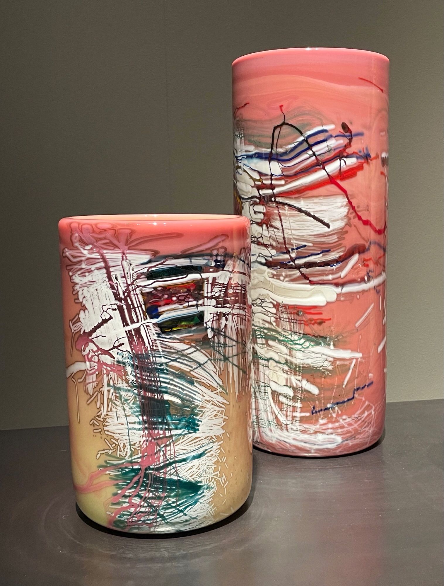 Two peachy-pink glass cylinders created by glass artist Dale Chihuly. Molten glass is rolled over glass threads to create a “pick up drawing”.