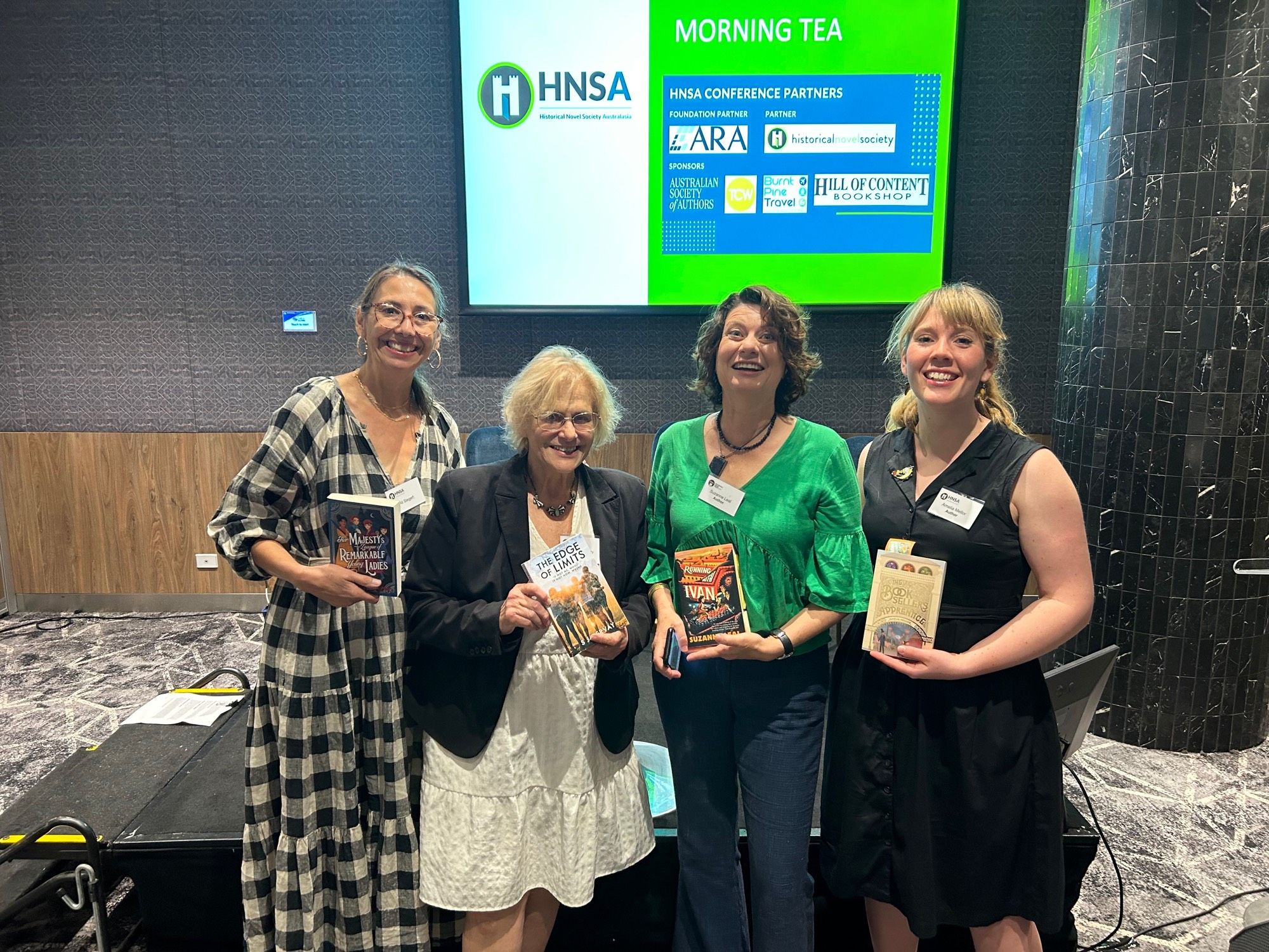 Four women holding books stand in front of a screen that says HNSA.