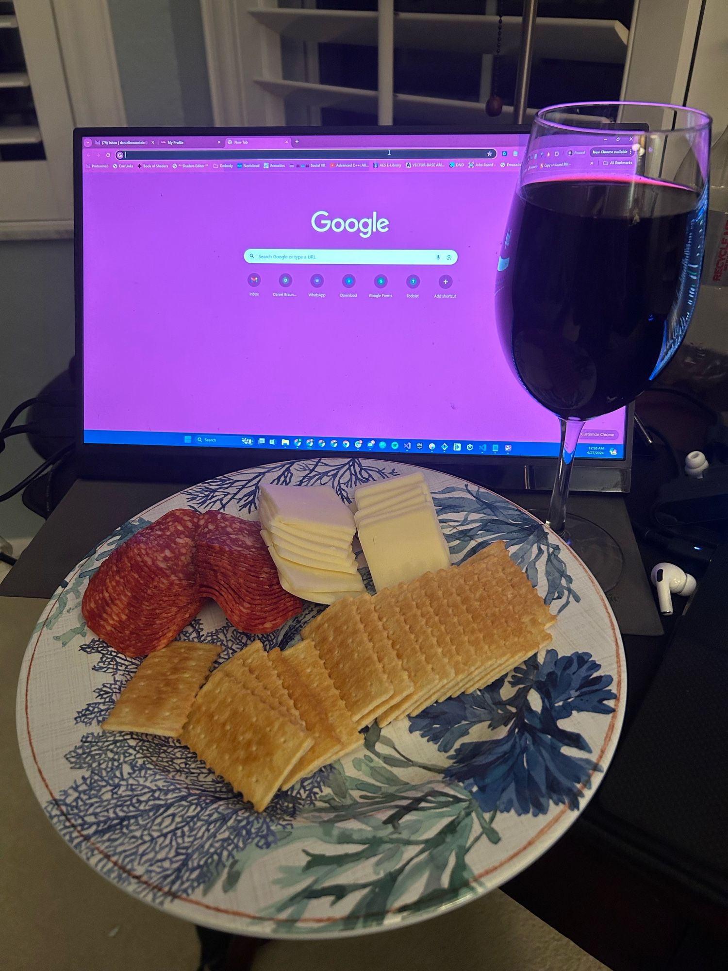 Pictured: a haphazard “charcuterie” plate with crackers, salami, and cheese; a computer monitor; and a comically overfilled glass of wine