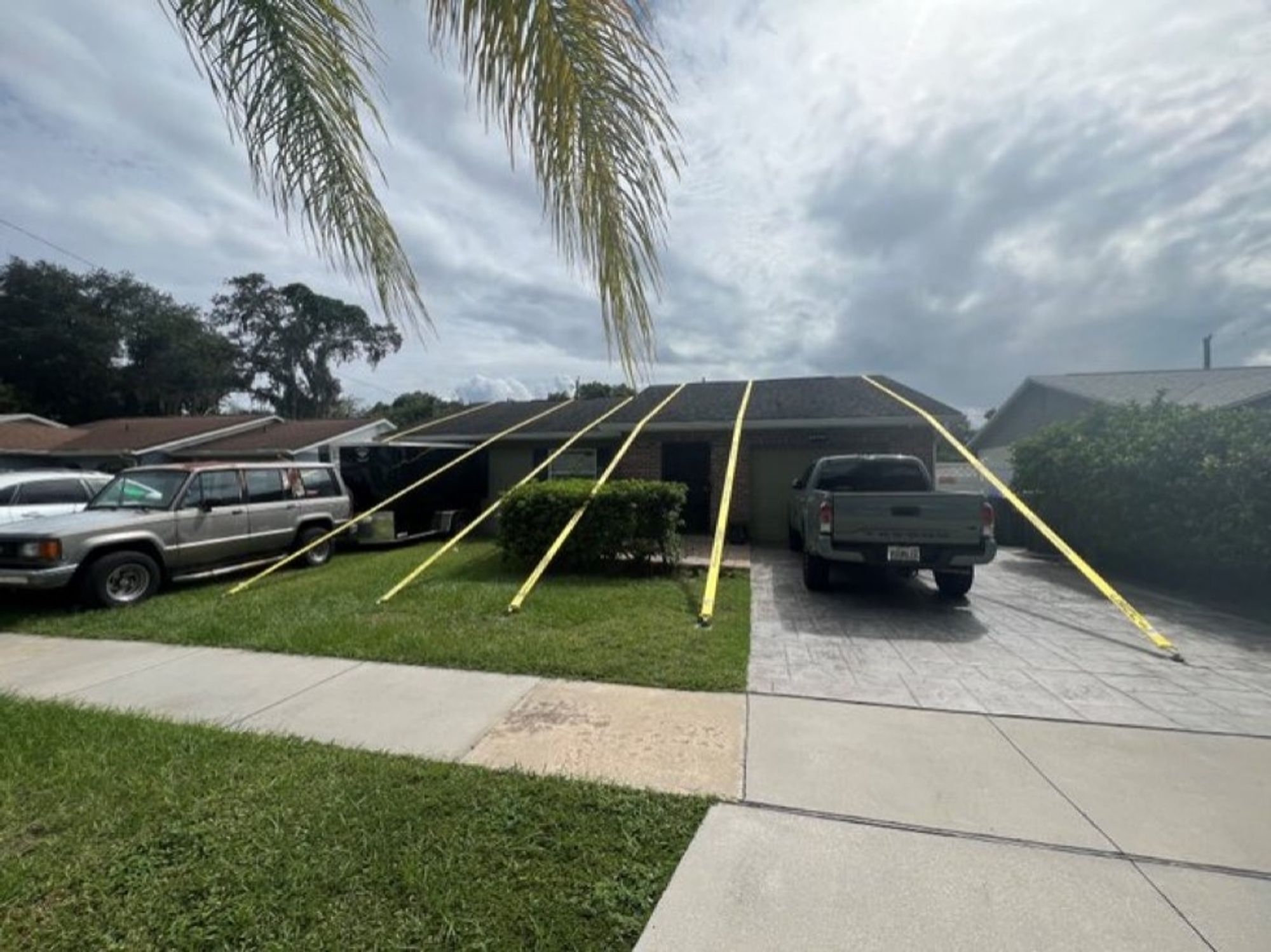 Maison en Floride avec pick-up up à droite et 2 autres grosses voitures à gauche.
La toiture  est maintenue par 4 sangles jaunes arrimées à la pelouse et une à l'allée béton.
Précaution prise en vue de l'ouragan Milton.