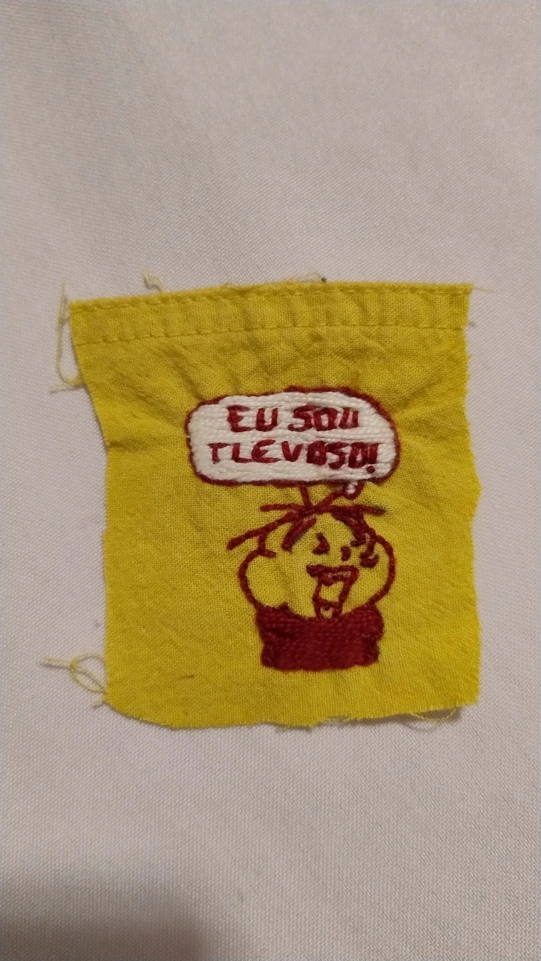 Bordado feito com fio vermelho em um retalho amarelo do Cebolinha vestido como um vampiro, com uma expressão dramática enquanto diz "eu sou tlevoso!". Referência: história O Cebolinha é um vampiro?, de onde veio o meme "Eu sou uma cliatula das tlevas atolmentada pela culpa e pela lejeição!"