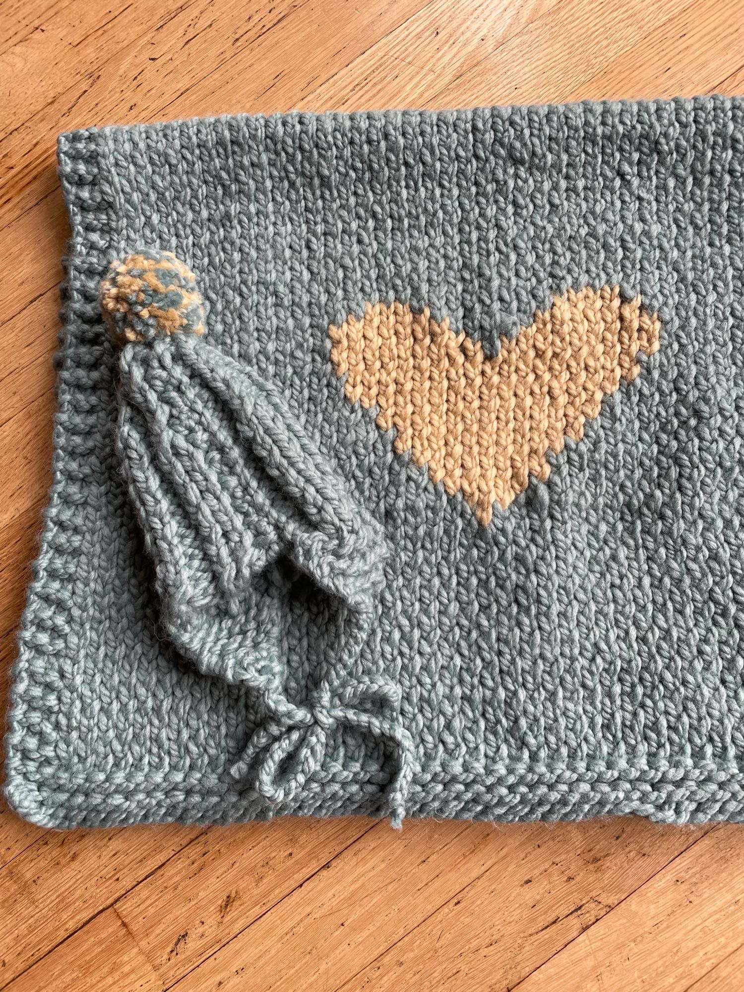 knitted grey-blue baby blanket with large beige heart and matching knitted hat