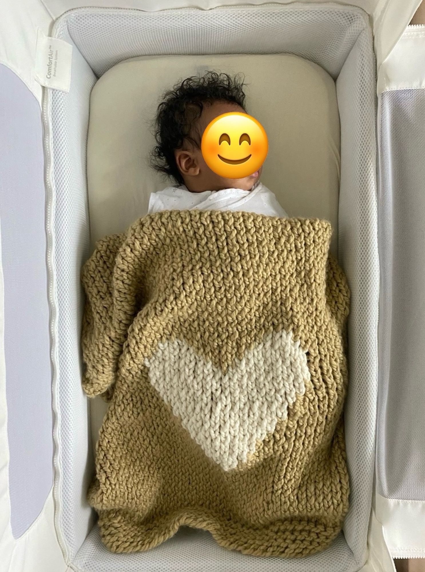 napping infant covered with sand-colored knitted blanket with large white heart