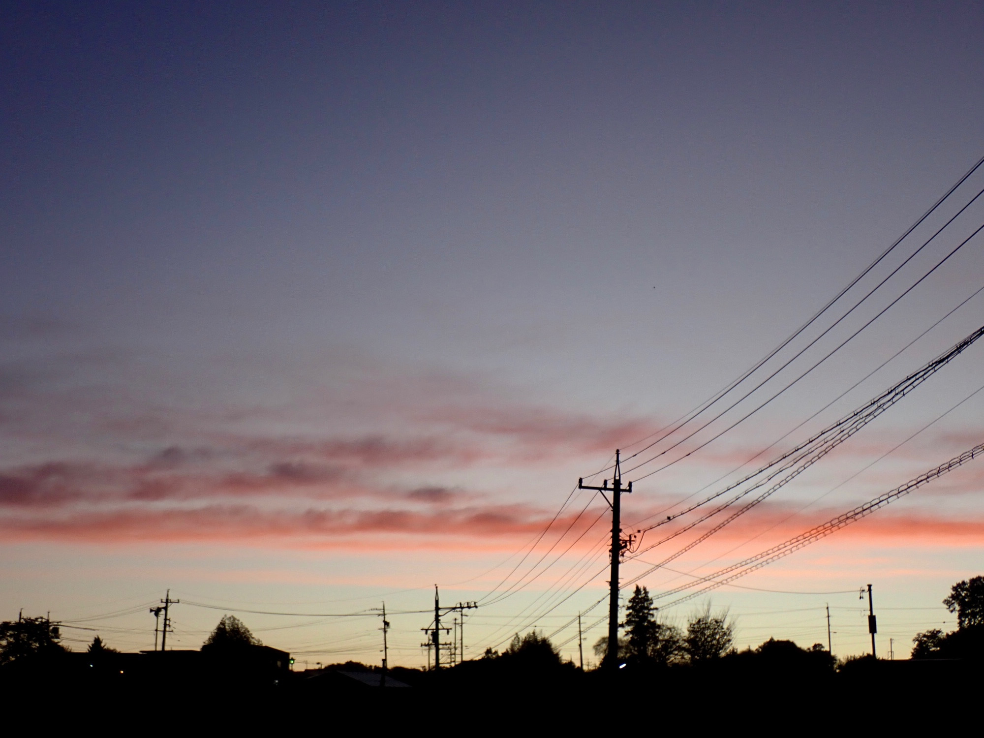 Morning scenery. Dark blue sky. Orange clouds in horizontal position above the horizon. Landscape in silhouette.