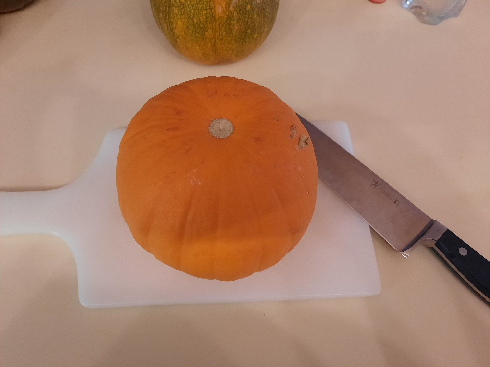 A small orange pie pumpkin on a cutting board next to a knife