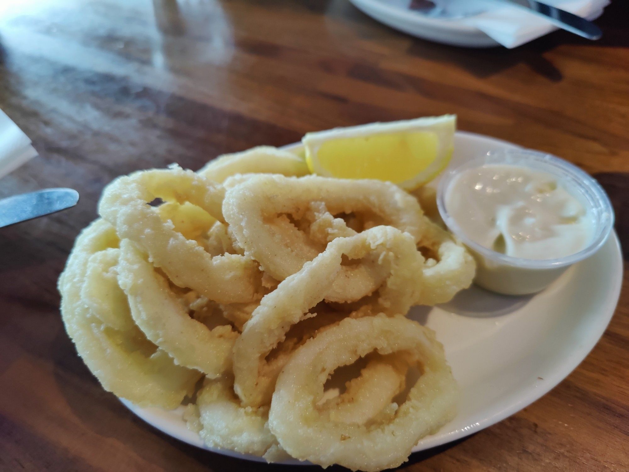 Deep fried calamari rings, a ramekin of garlic mayonnaise is on the plate and a slice of lemon