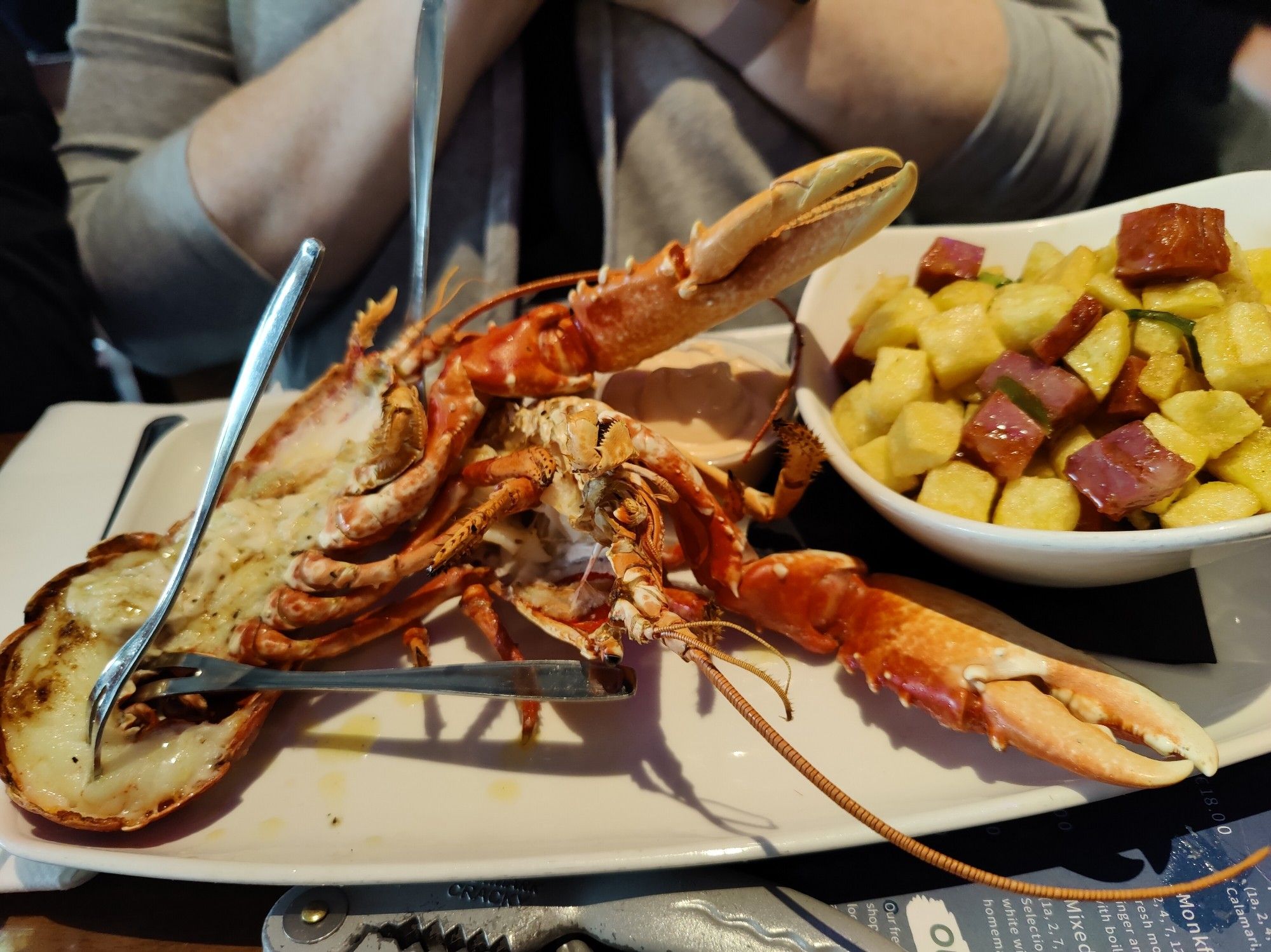 A whole split lobster. A side of potatoes and chorizo is to the right